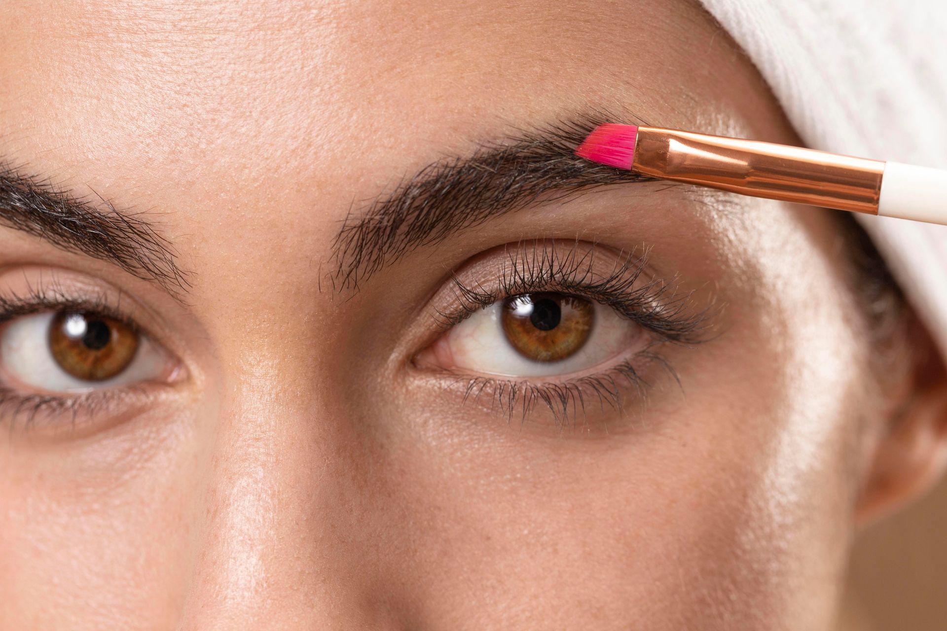 A woman is applying makeup to her eyebrows with a brush.