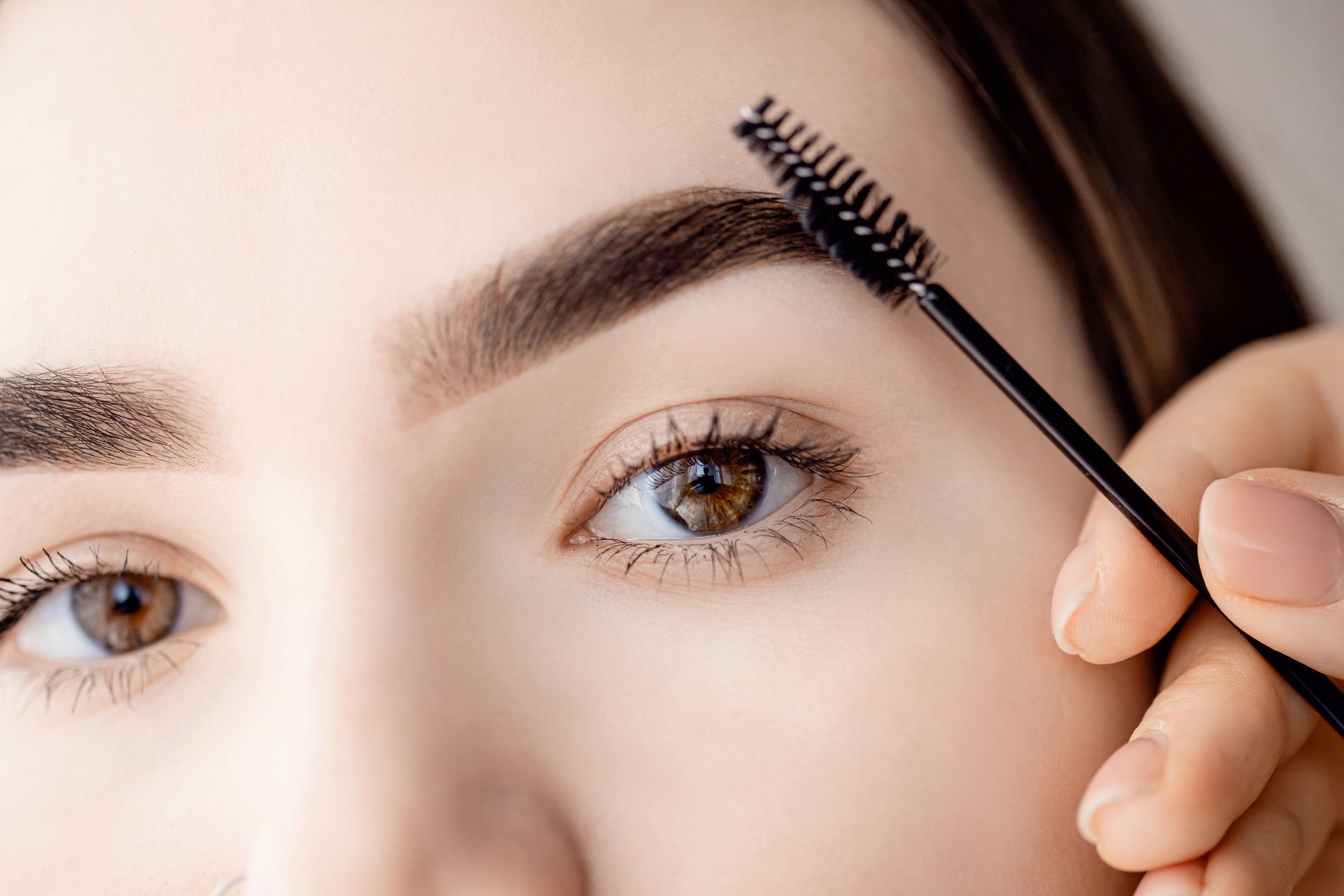 A woman is brushing her eyebrows with a brush.