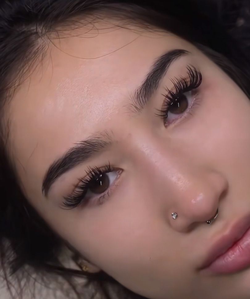 A close up of a woman 's face with long eyelashes and a nose ring.