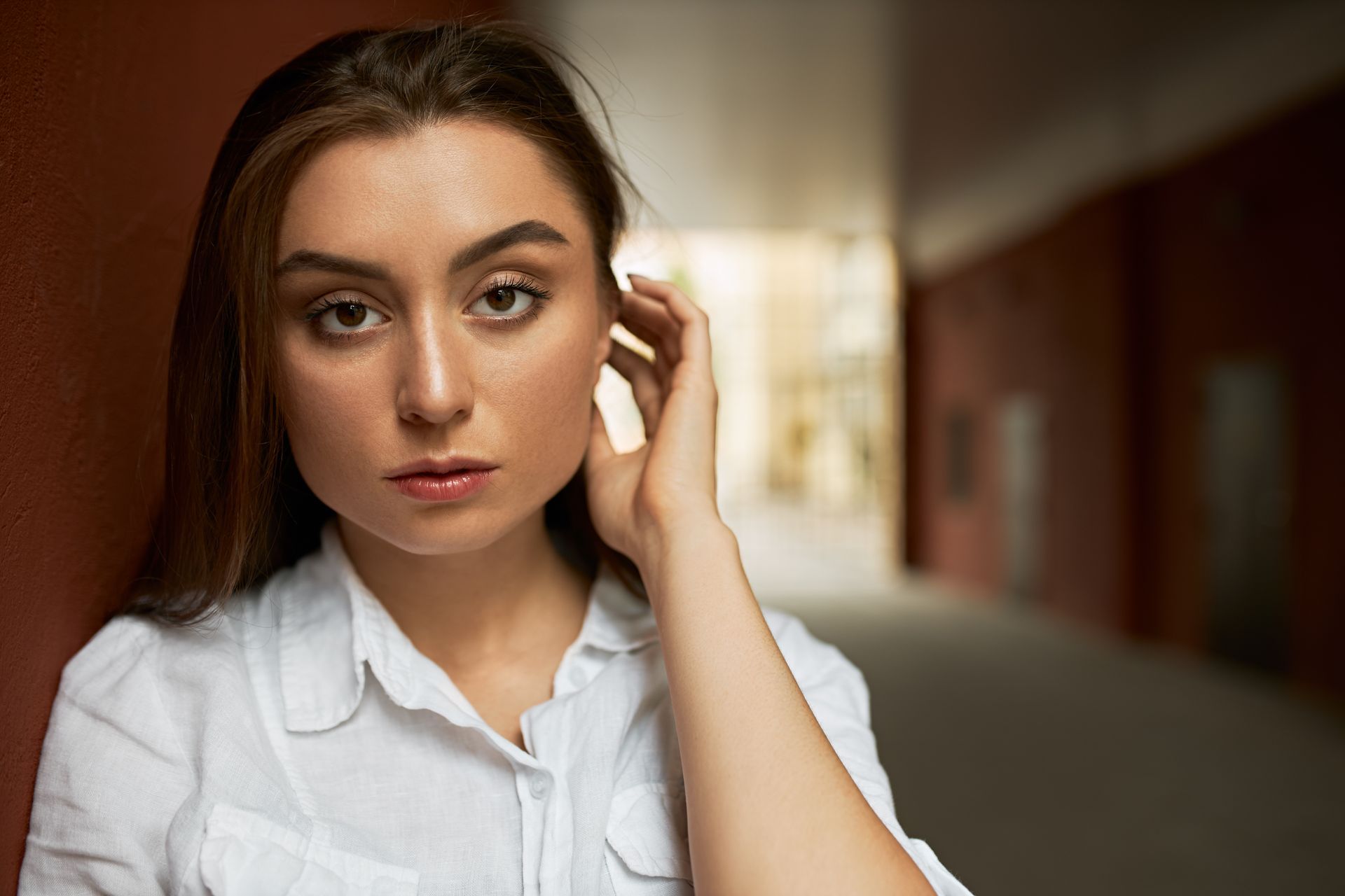 A woman in a white shirt is holding her hand to her ear.