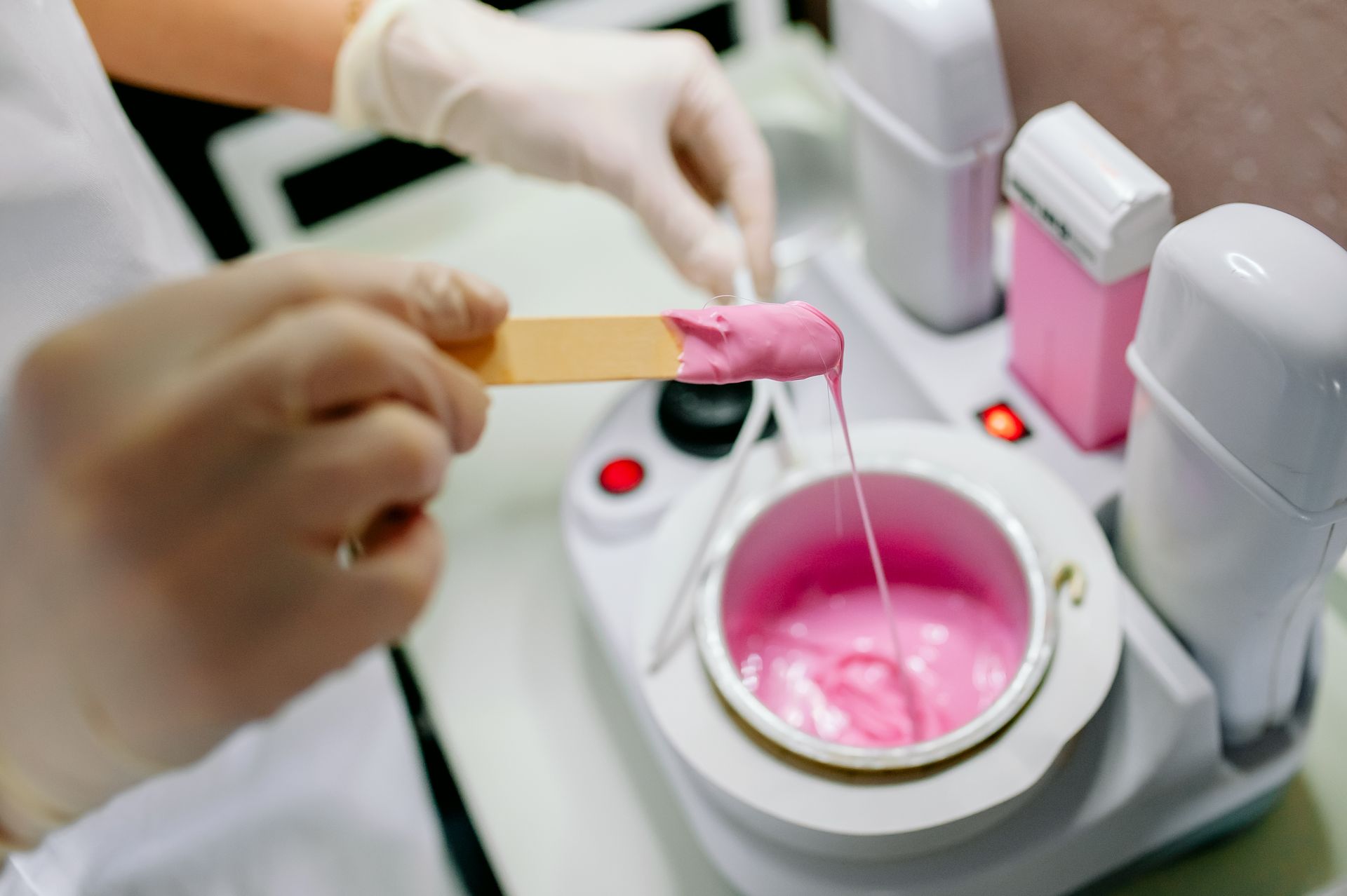 A person is applying wax to a stick in a wax warmer.