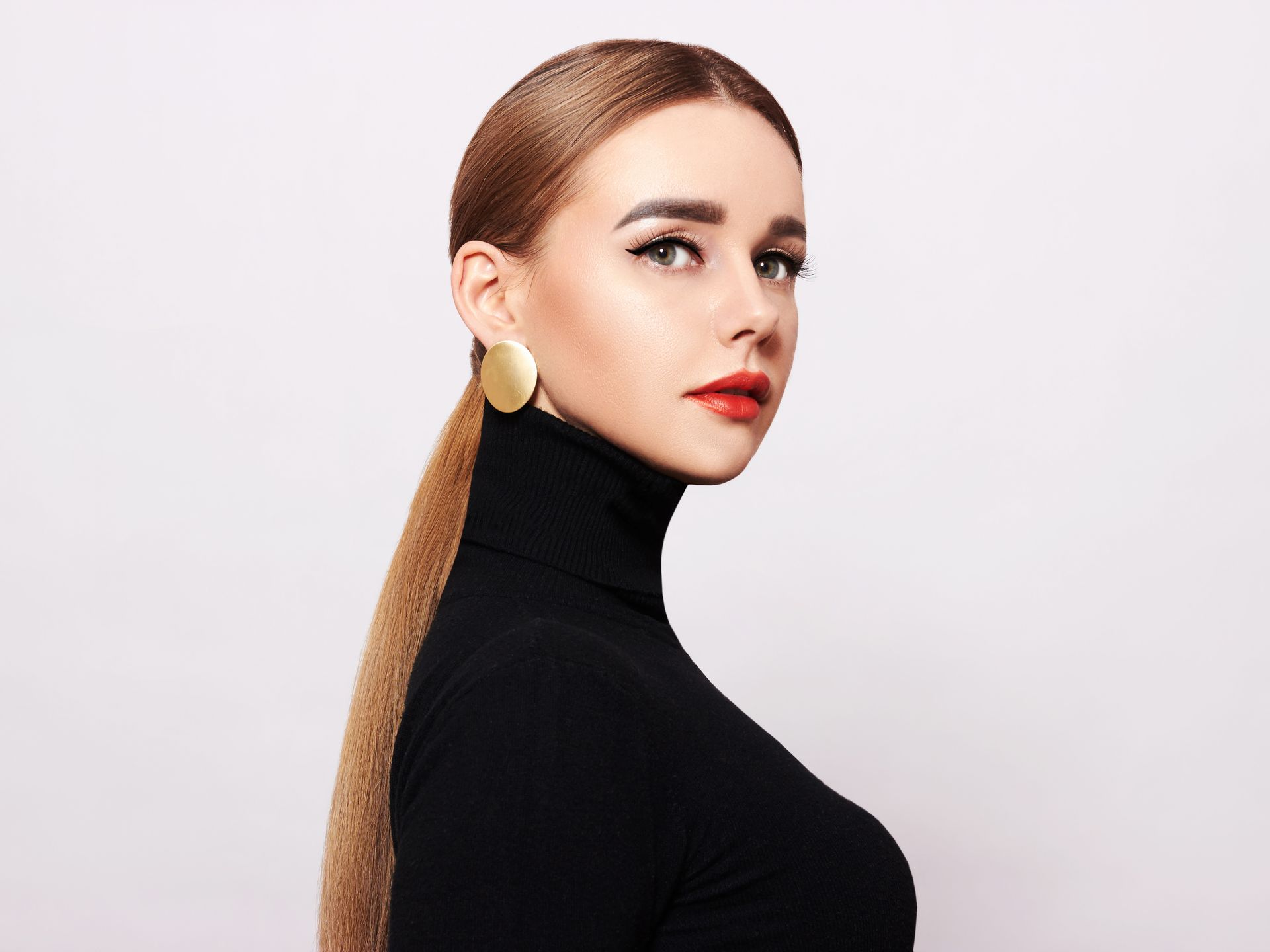 The woman is wearing a black turtleneck and gold earrings.