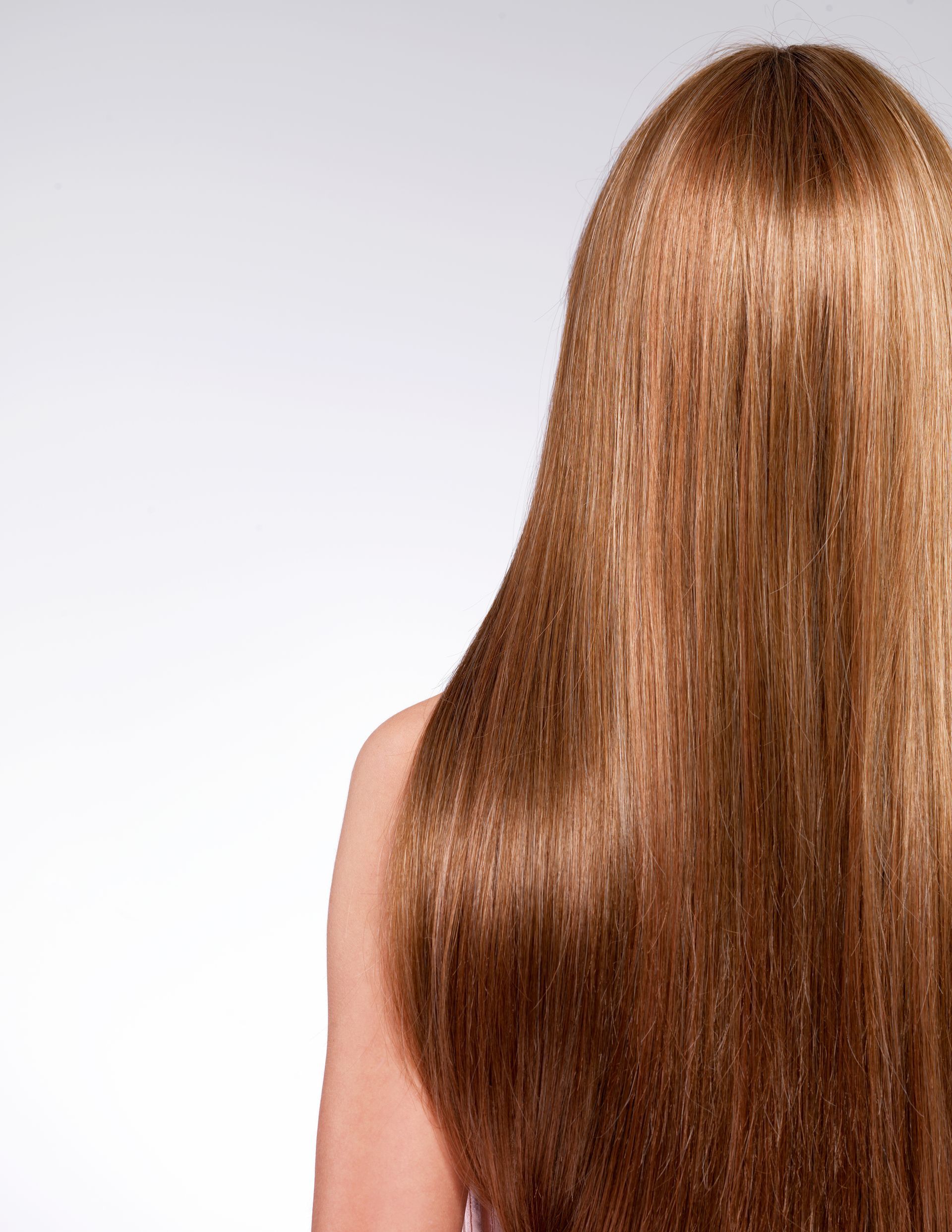 A woman with long brown hair is standing in front of a white background.