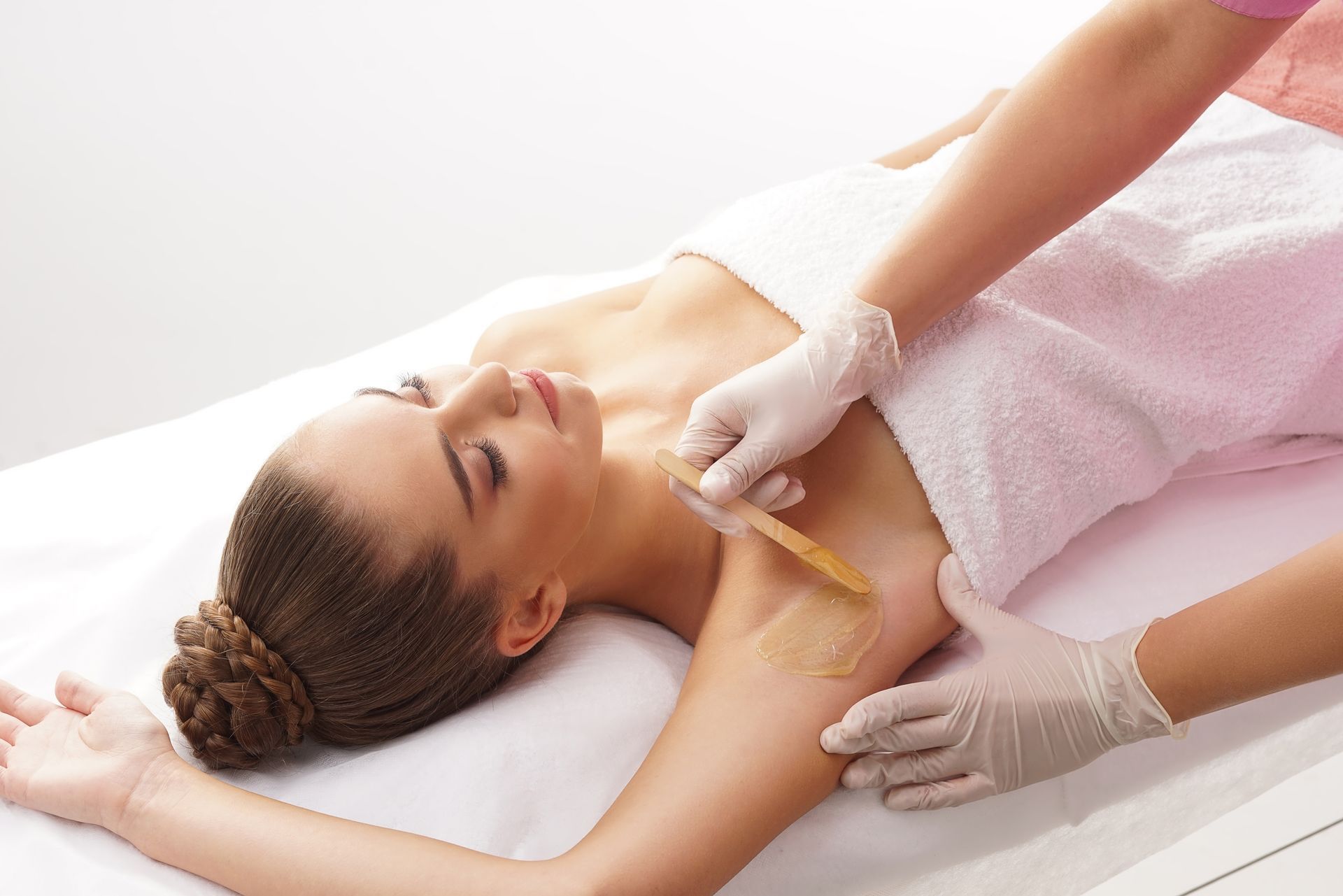 A woman is laying on a bed getting her armpit waxed.