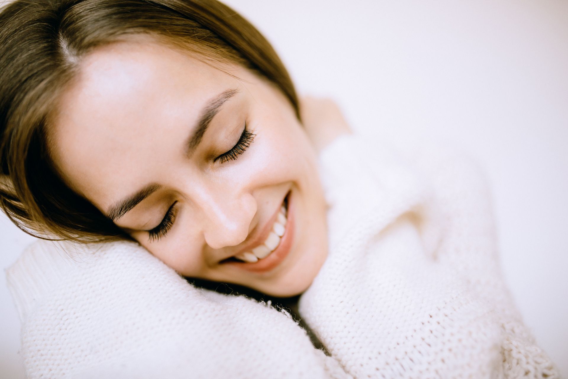 A woman in a white sweater is smiling with her eyes closed.