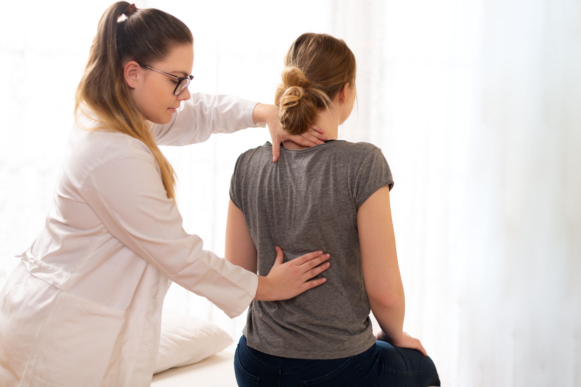 A chiropractor assessing patient posture and spine alignment during a back exam in a clinic room
