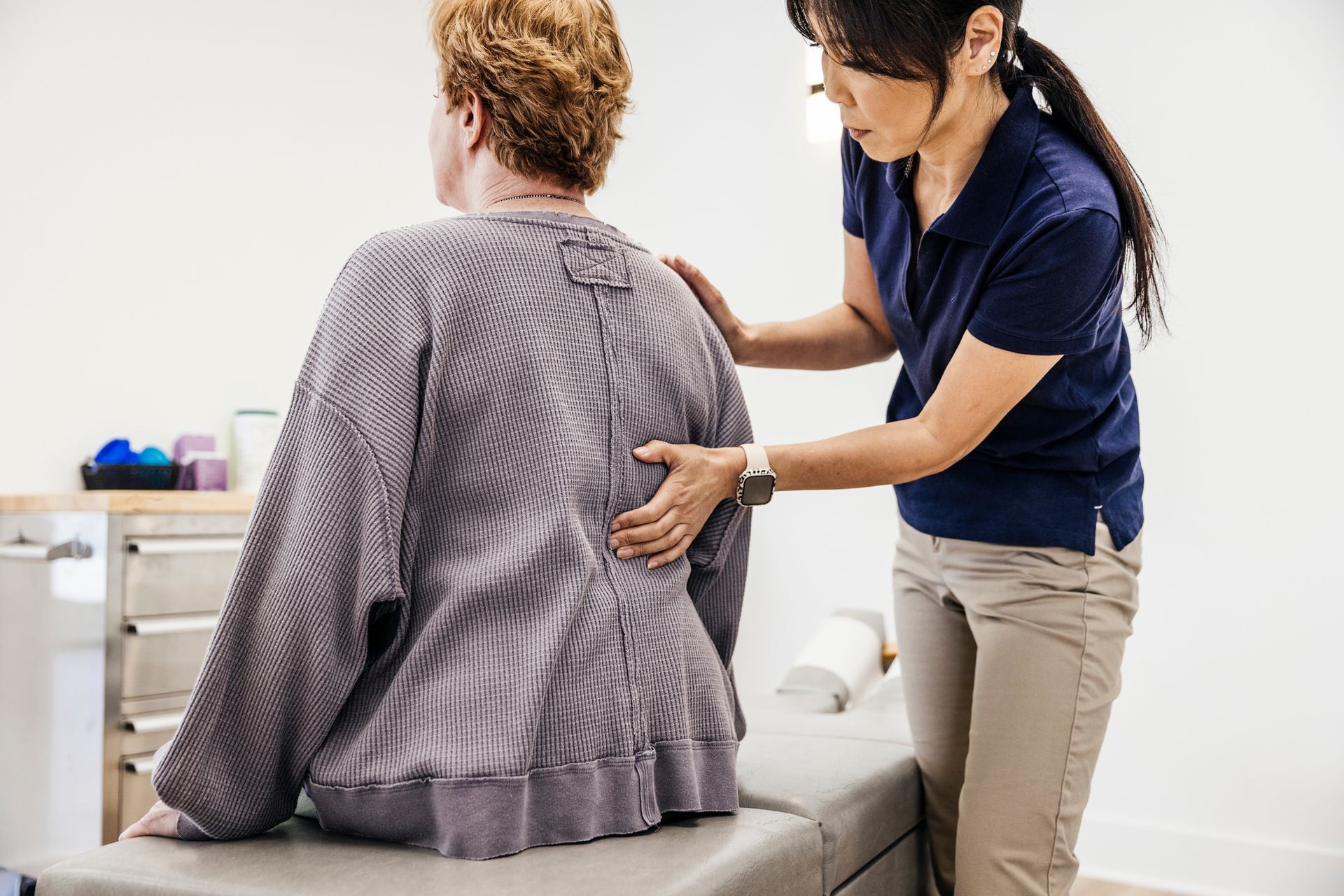 Chiropractor assessing senior woman’s spine during a clinic visit.