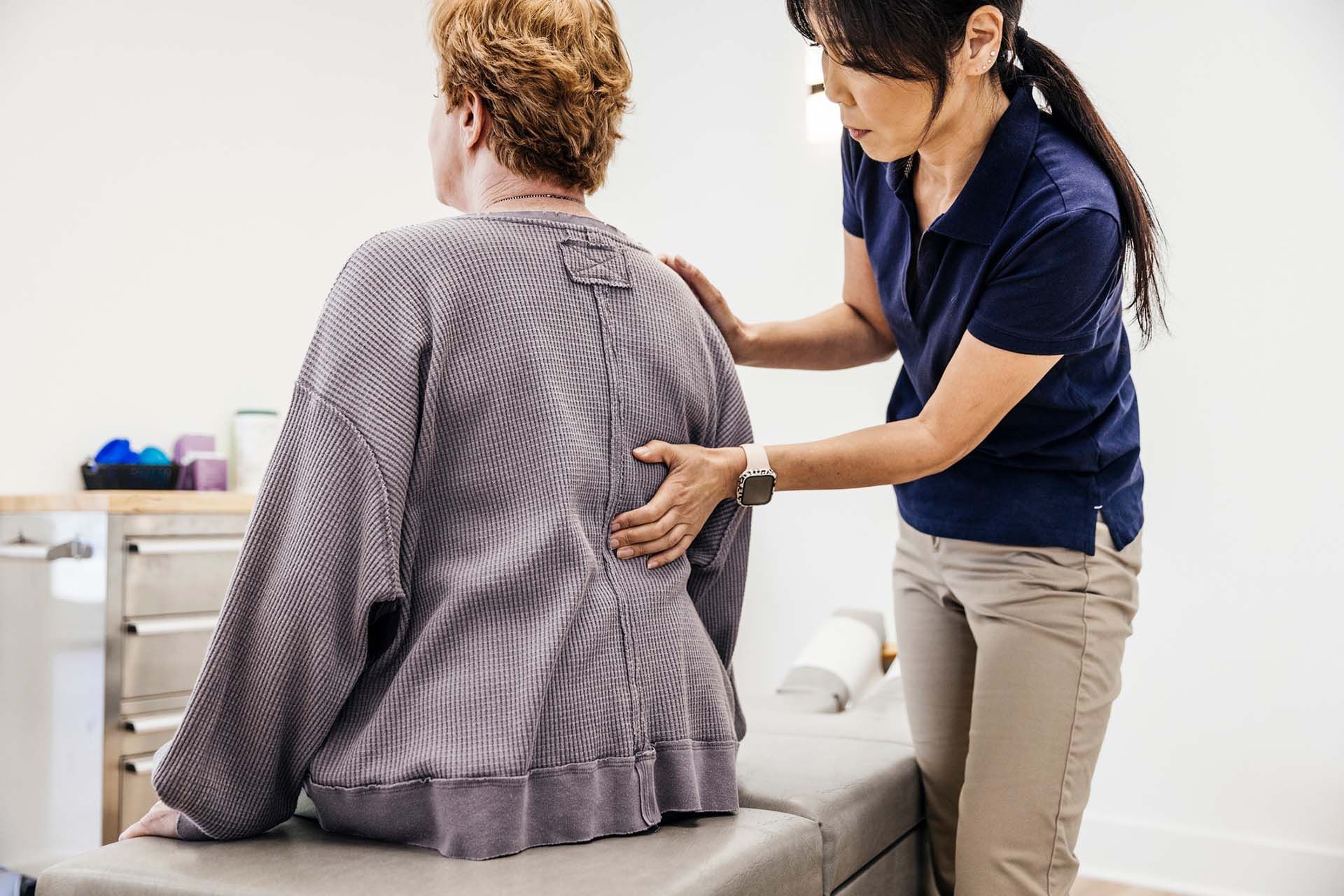 A female clinician examines patient's lower back in medical office setting.