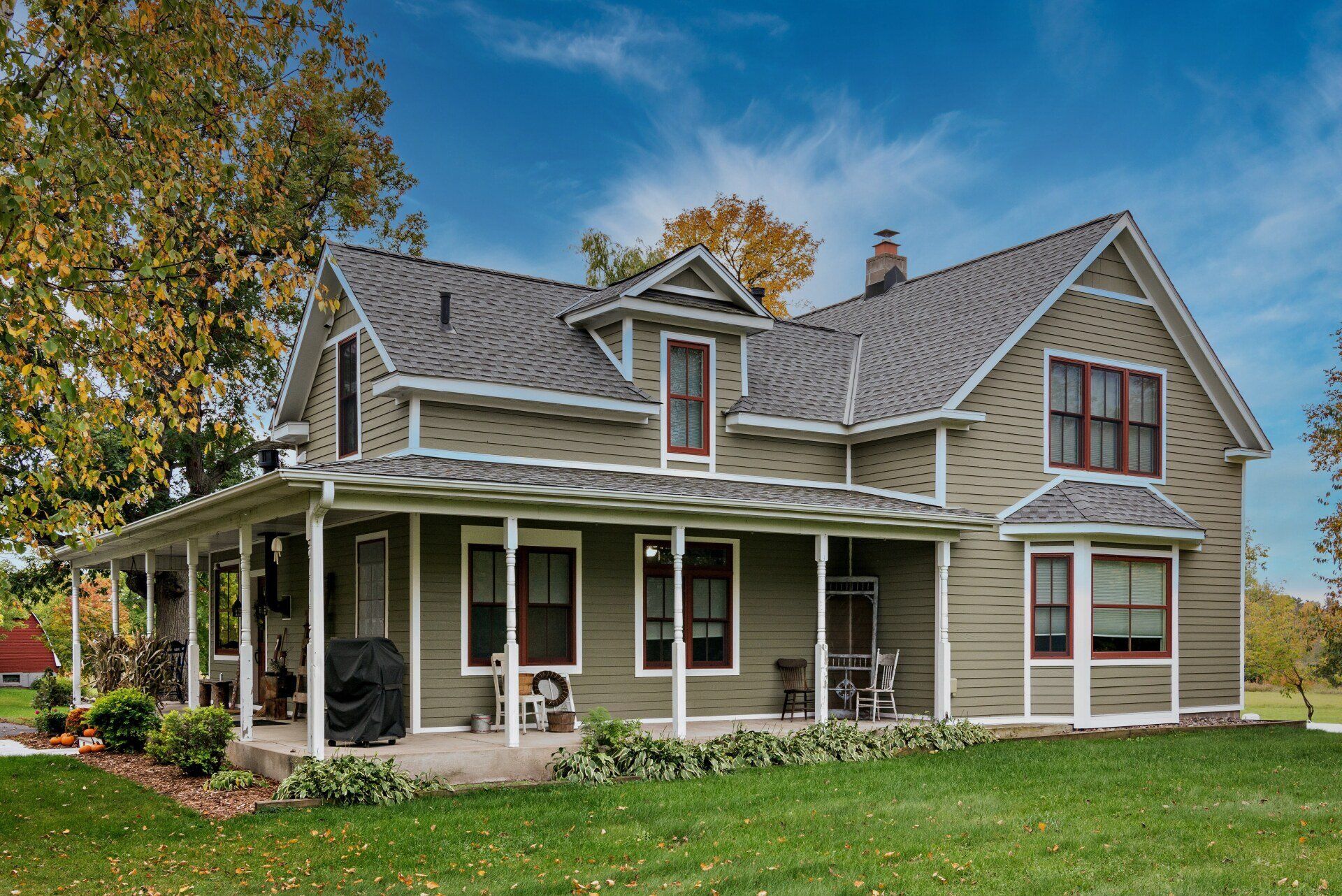A large house with a large porch is sitting on top of a lush green field.