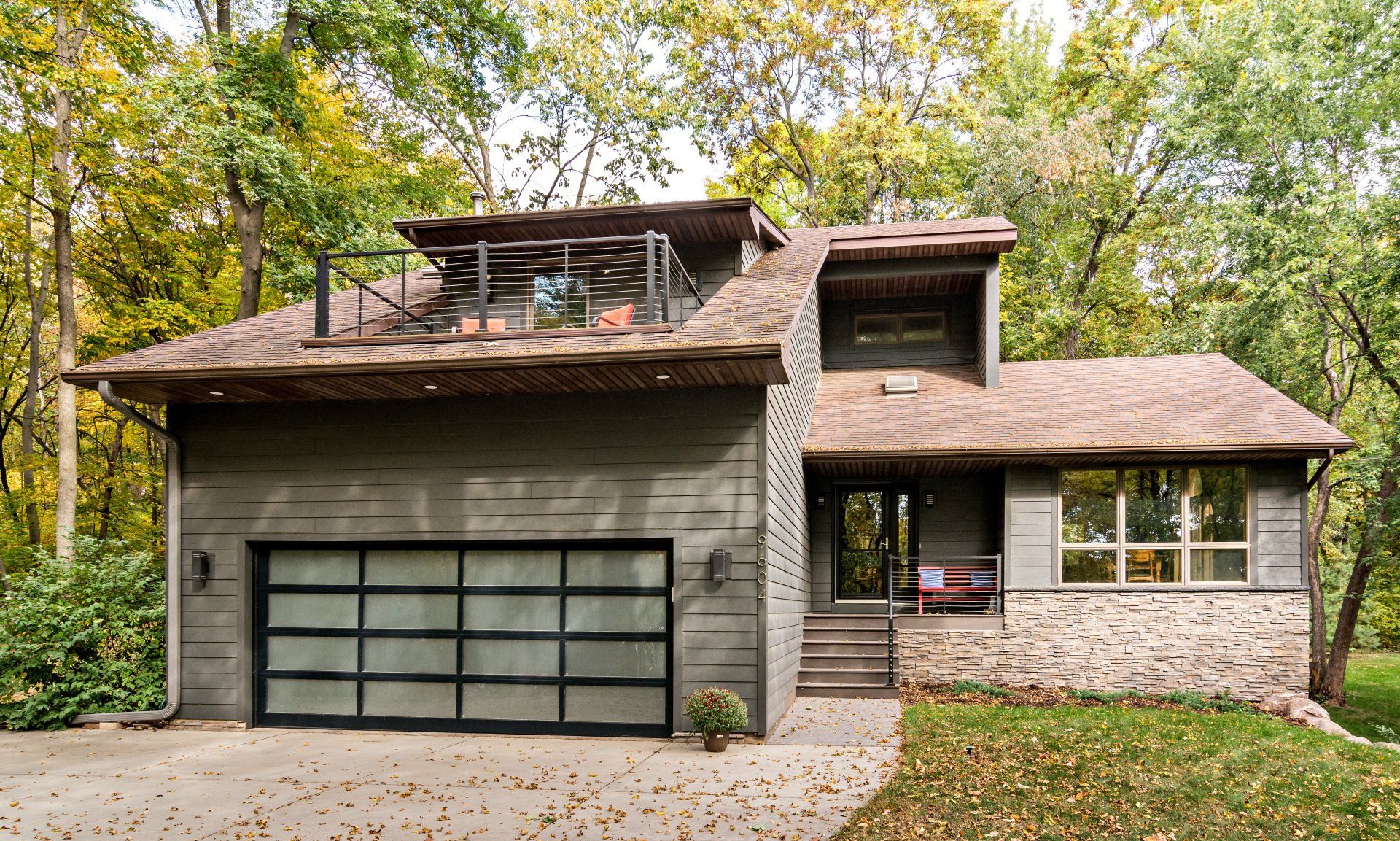 A modern house with a large garage door is surrounded by trees.