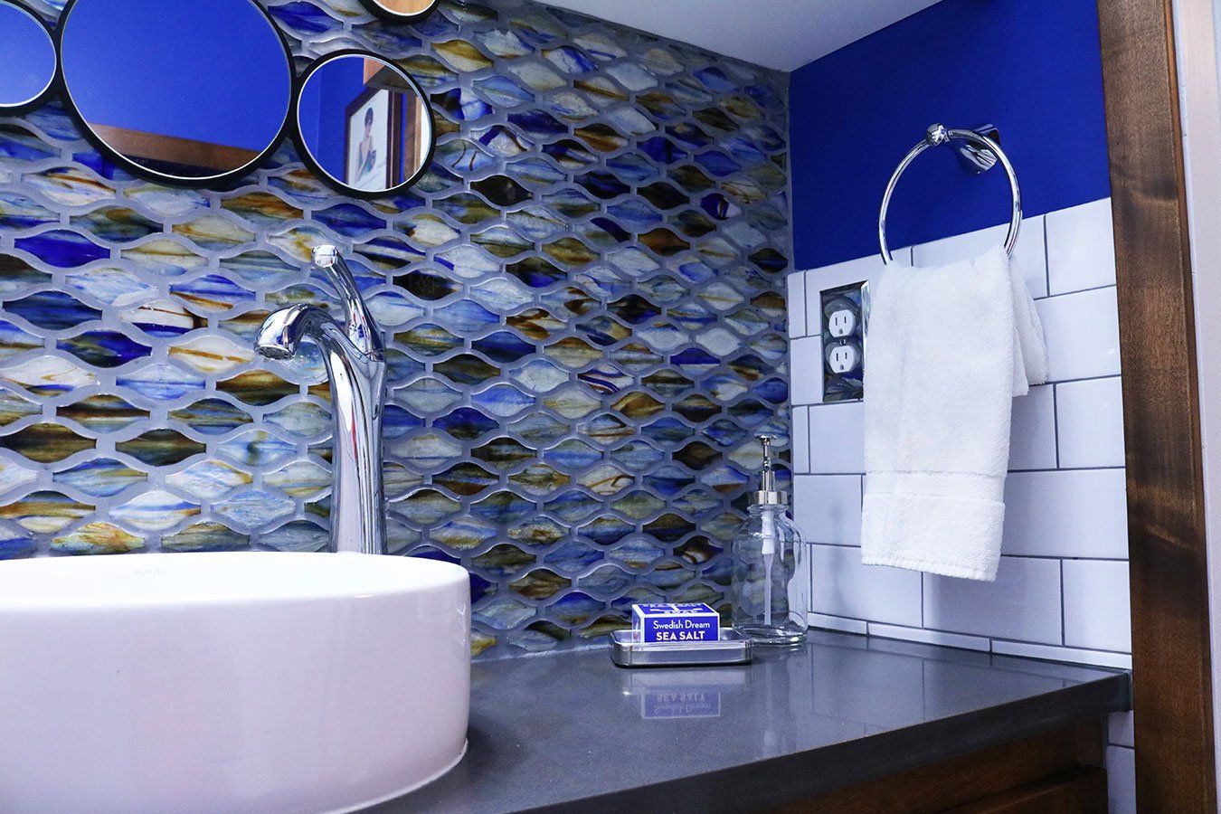 A bathroom with a sink , mirrors and blue tiles.