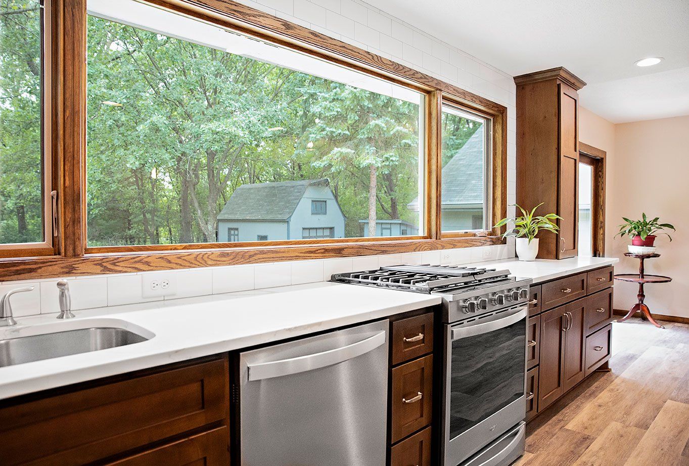A kitchen with a stove , sink , dishwasher , and large window.