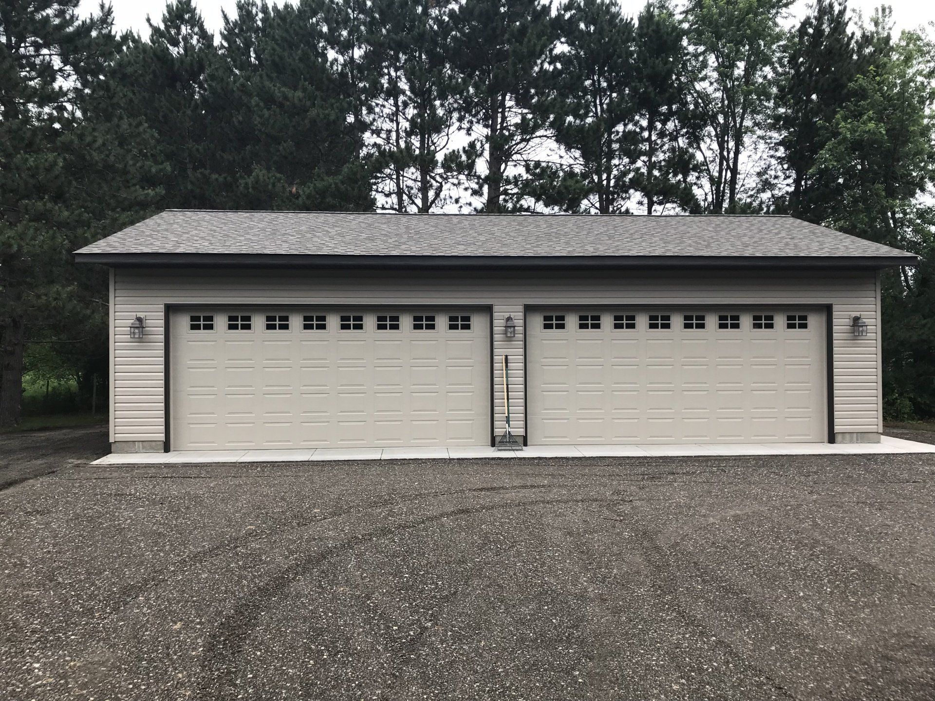 A large garage with two garage doors is surrounded by trees.