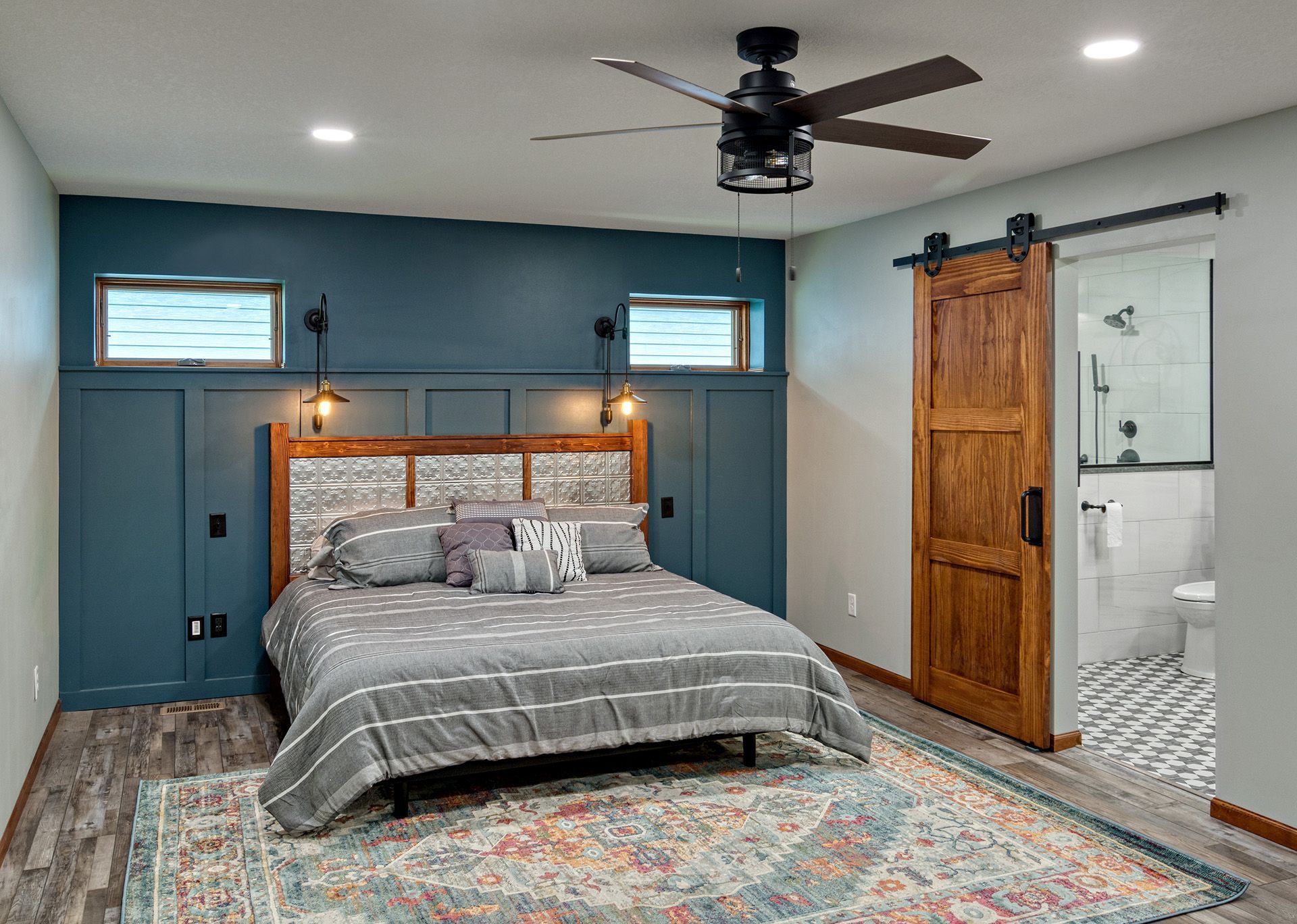 A bedroom with a bed , rug , ceiling fan and sliding barn door.