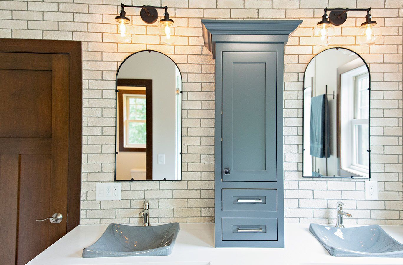 A bathroom with two sinks , a cabinet , and two mirrors.