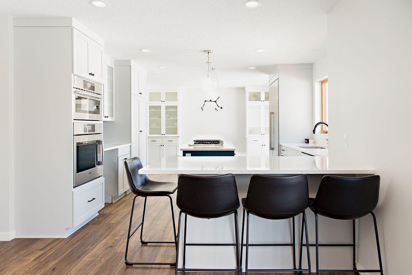 A kitchen with white cabinets , black chairs , and a large island.