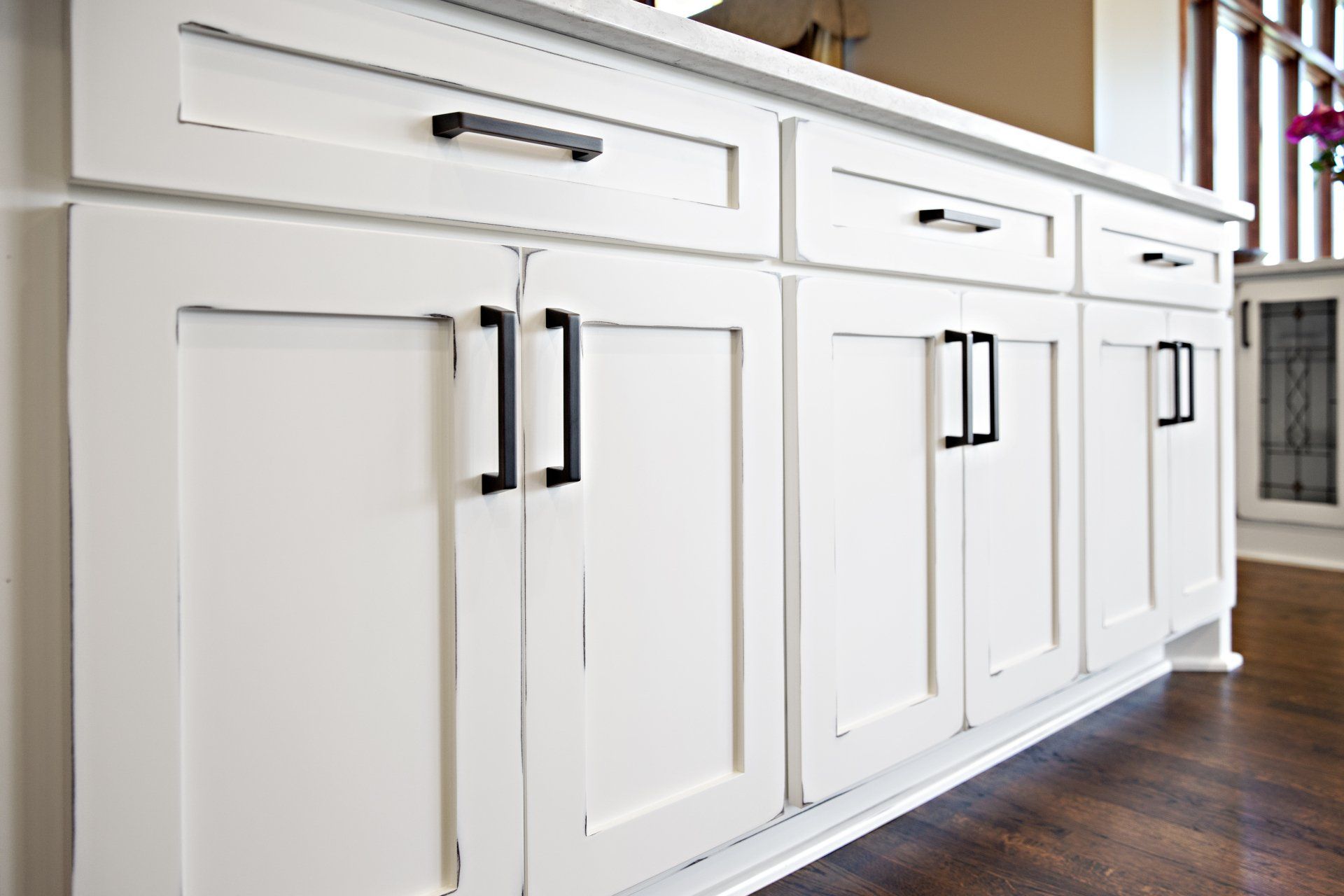A kitchen with white cabinets and black handles.
