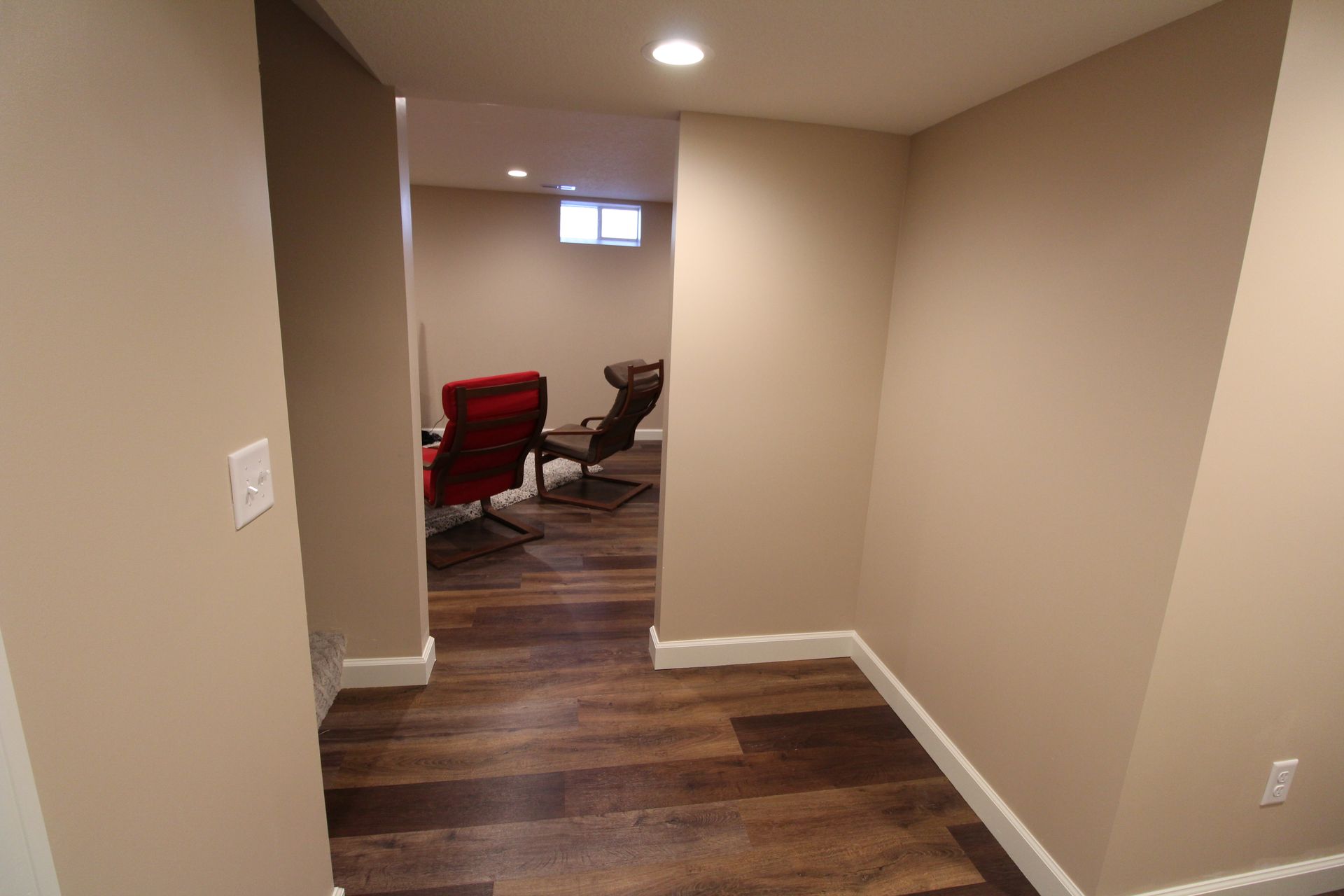 A hallway in a basement with hardwood floors and chairs.