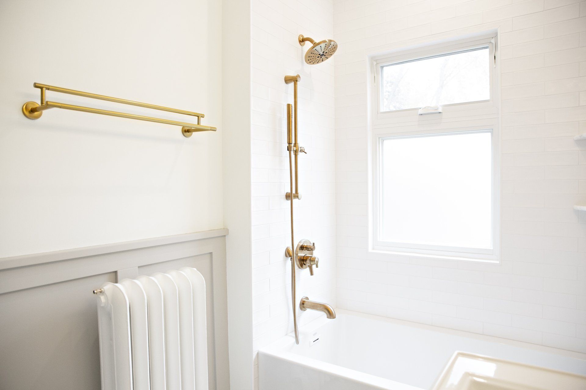 A bathroom with a bathtub , shower , window and towel rack.