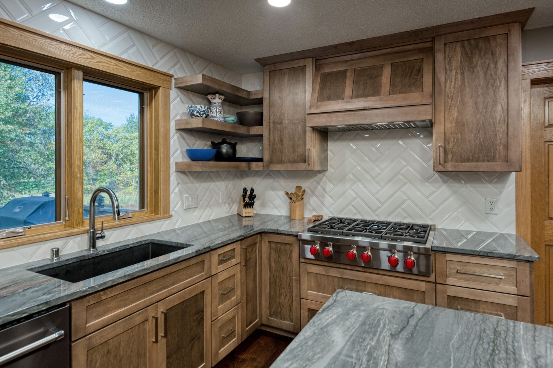 A kitchen with wooden cabinets , granite counter tops , a stove and a sink.