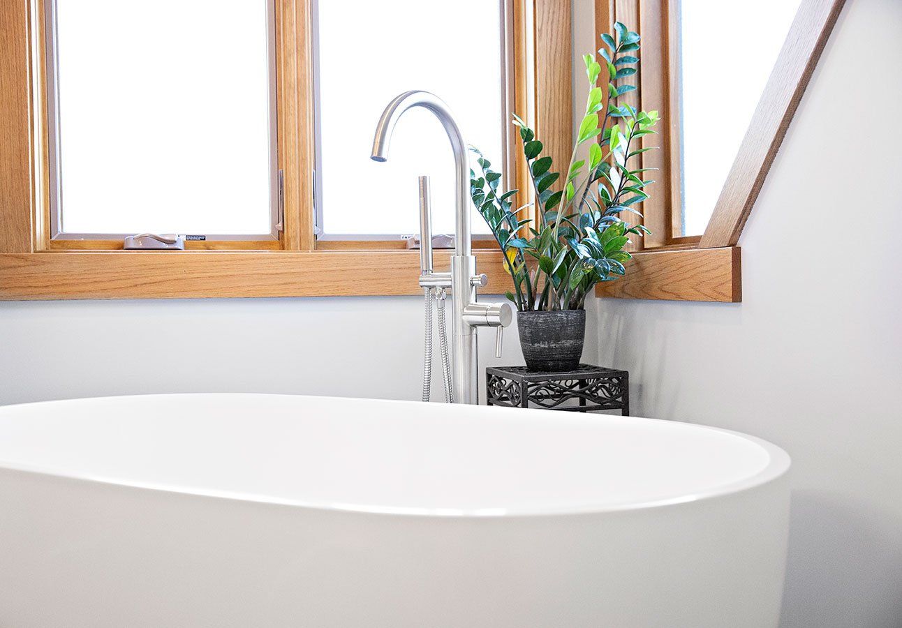 A bathtub with a faucet and a potted plant in front of a window.