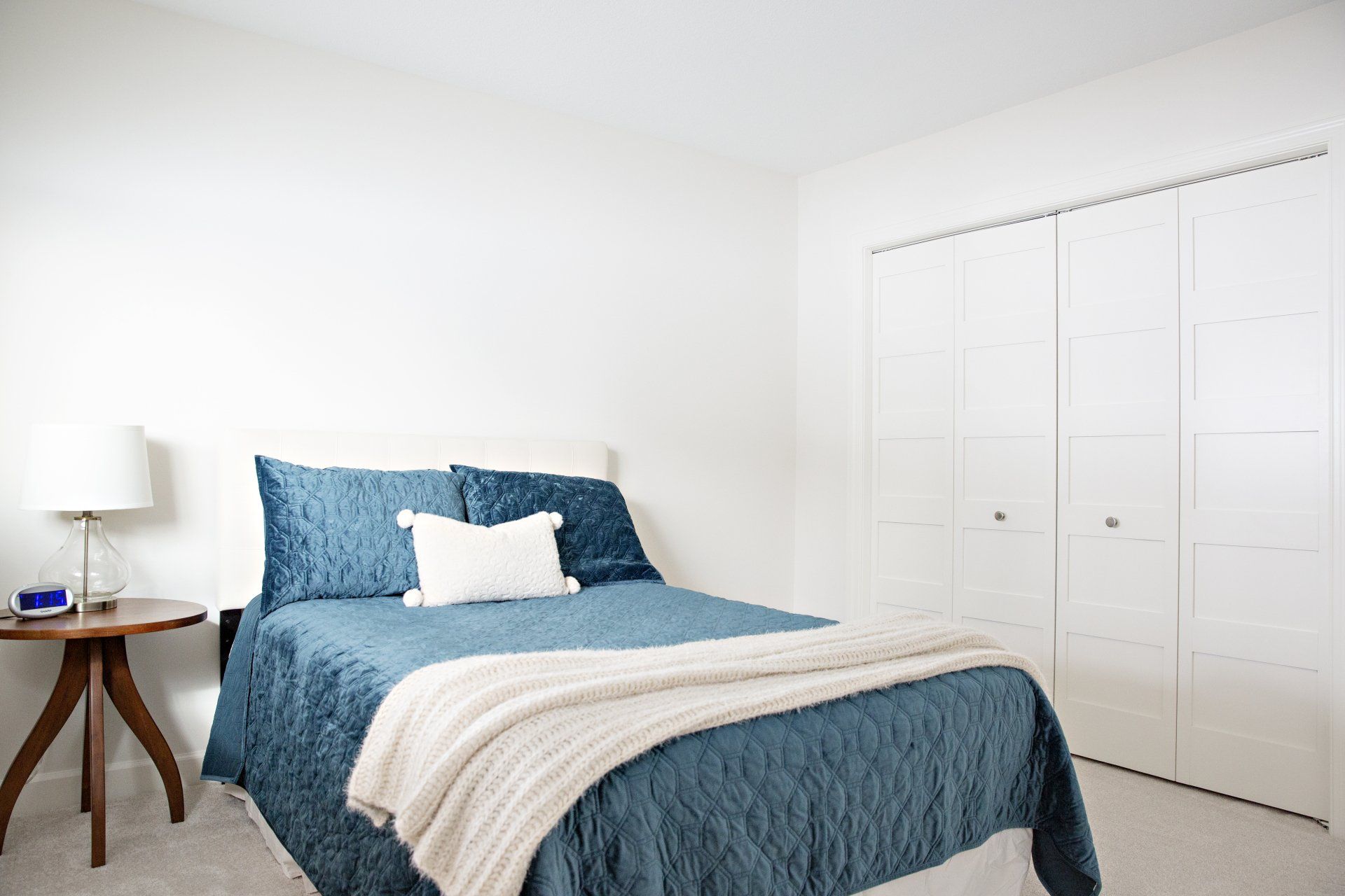 A bedroom with a bed , nightstand , lamp and closets.