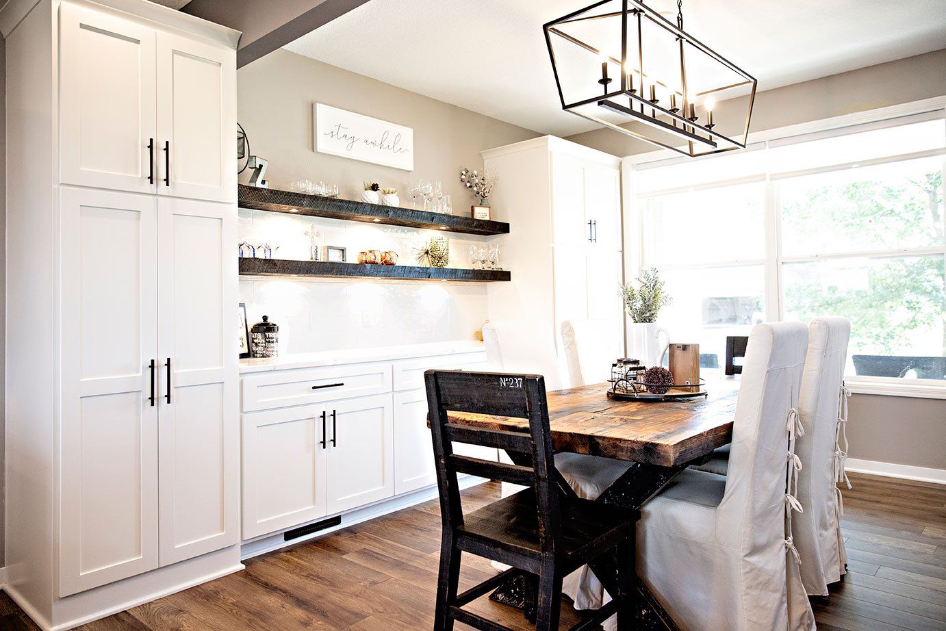 A dining room with a wooden table and chairs and white cabinets.