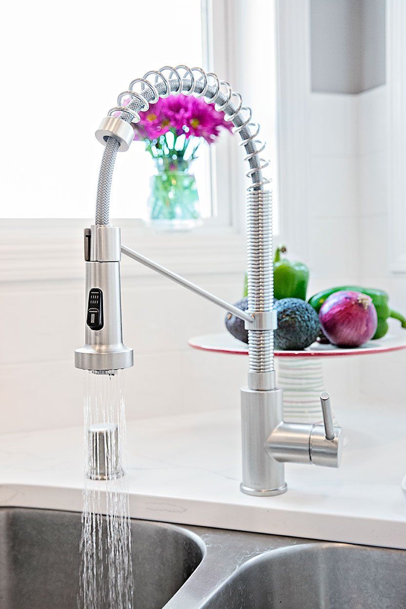 A kitchen sink with a faucet and a vase of flowers on the counter.