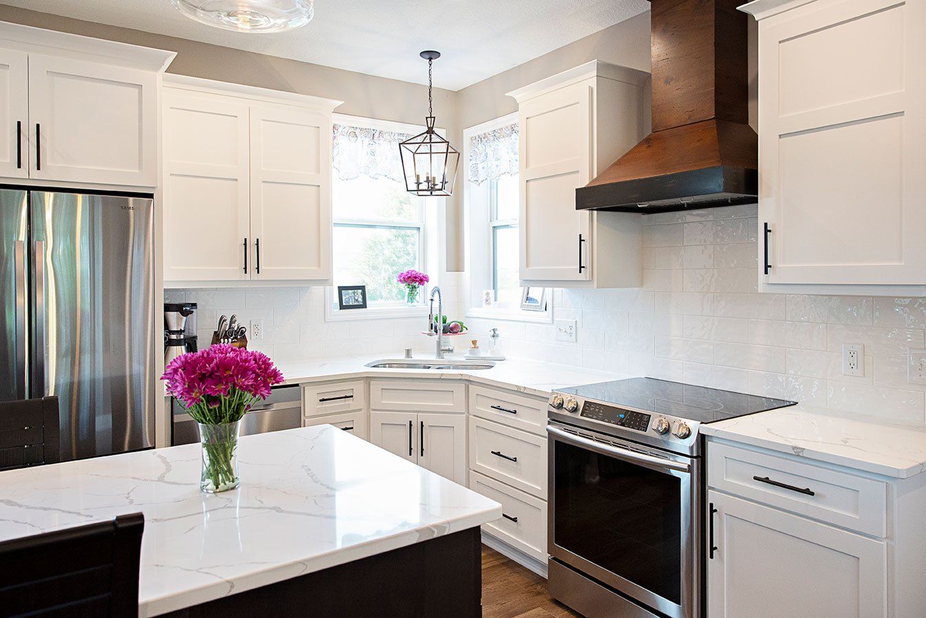 A kitchen with white cabinets , stainless steel appliances , and a vase of flowers on the counter.