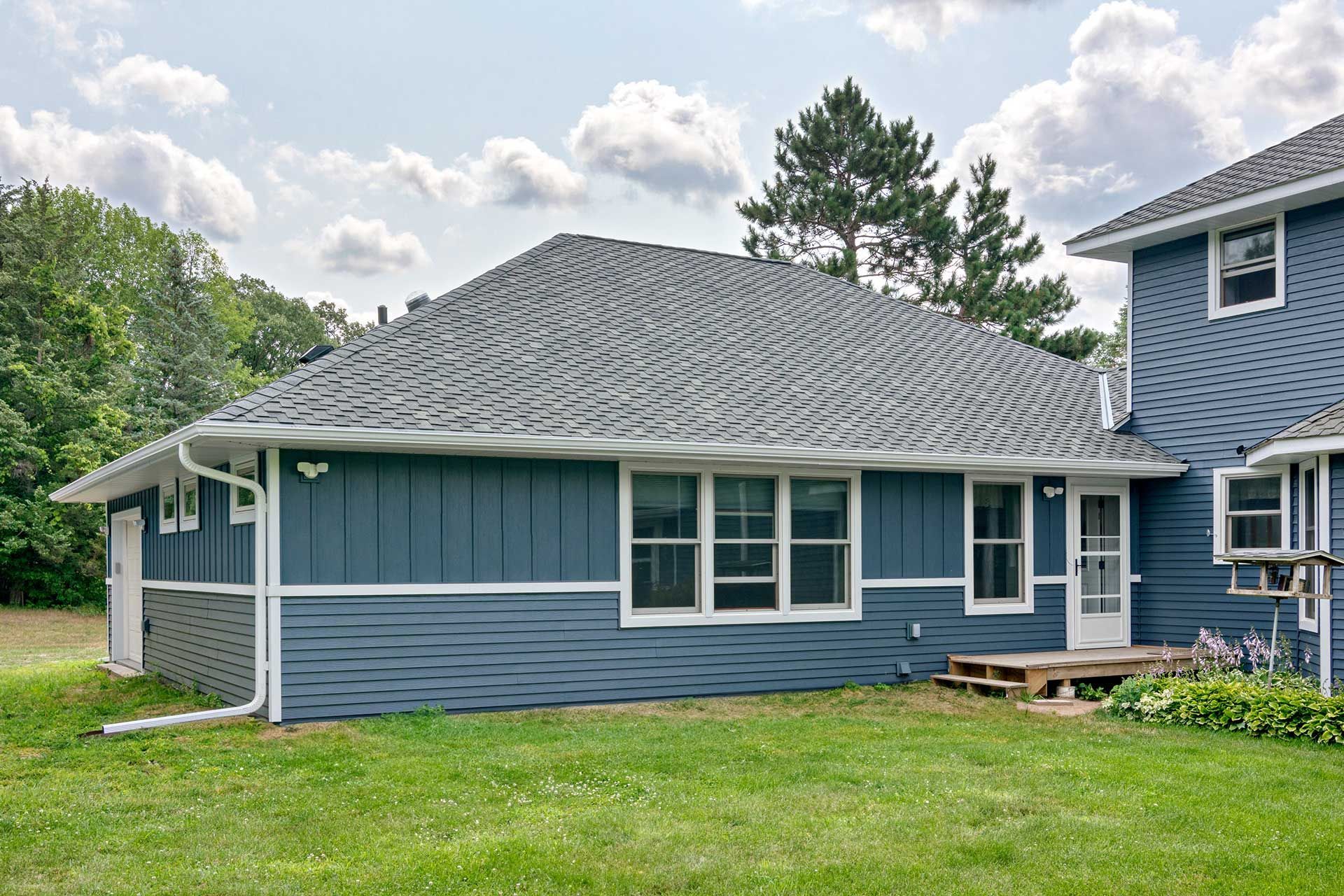 A blue house with a gray roof is sitting on top of a lush green field.