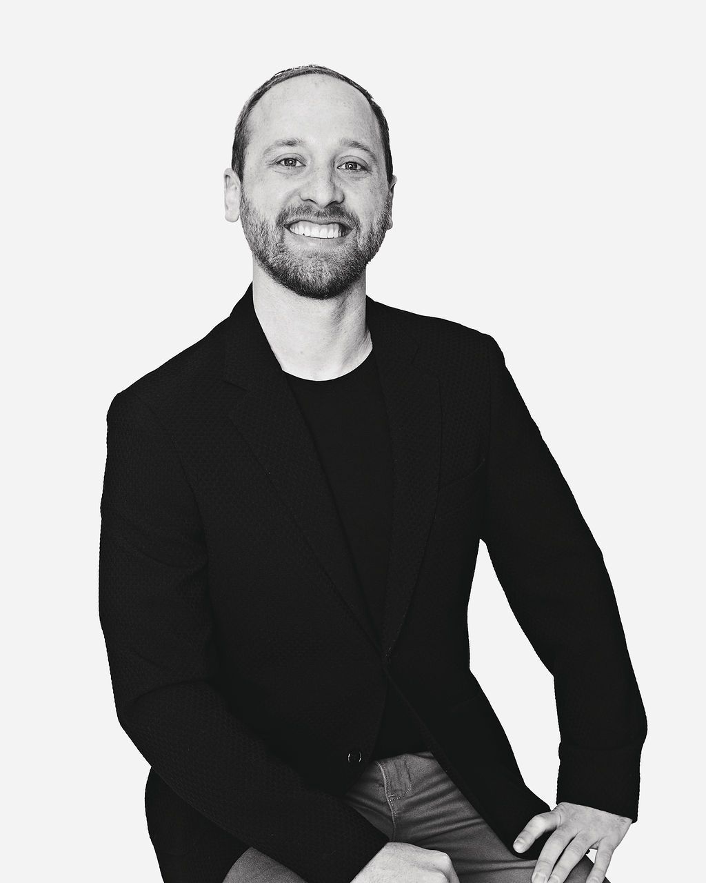 A man with a beard is wearing a black jacket and smiling