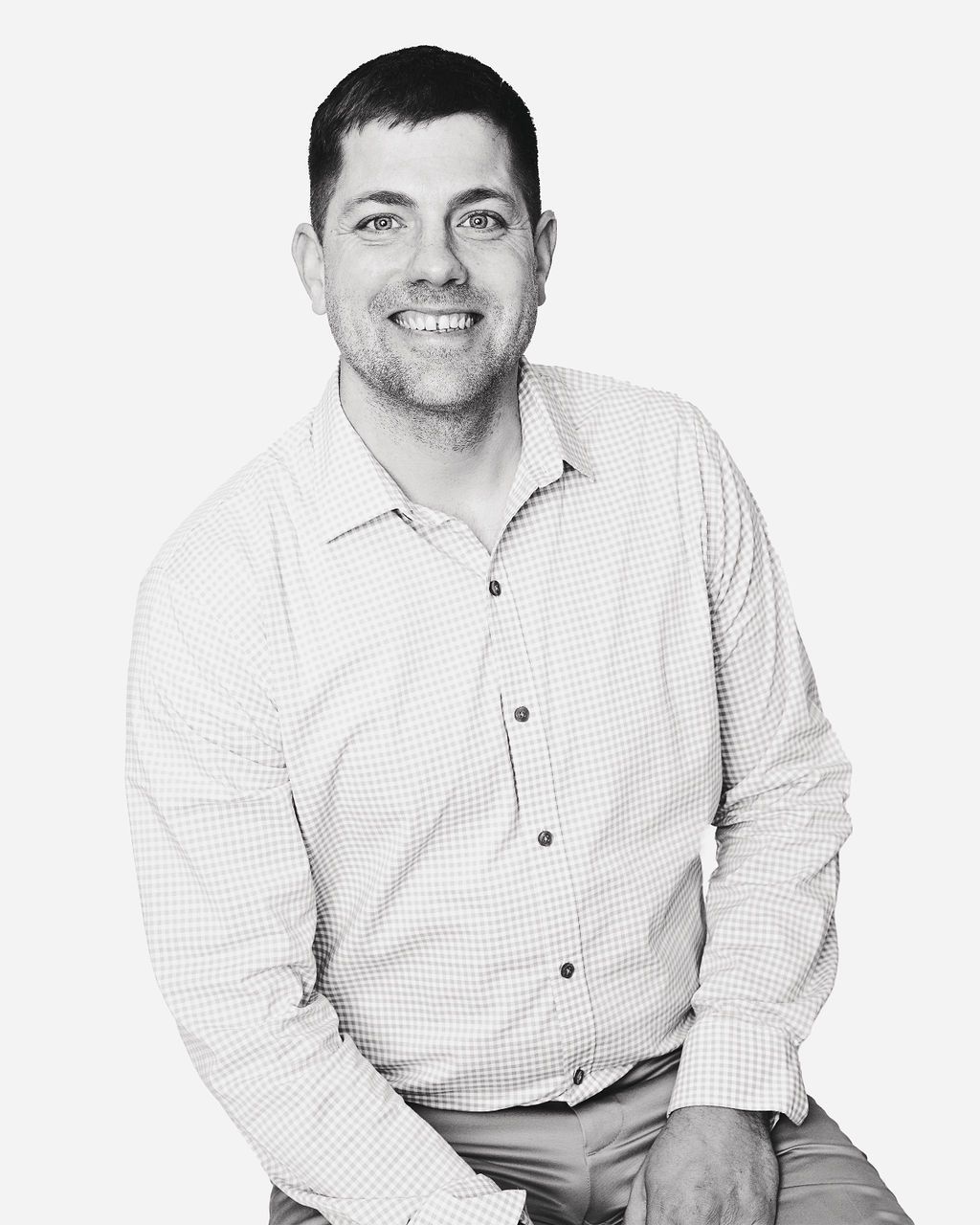 A man in a white shirt is smiling in a black and white photo.