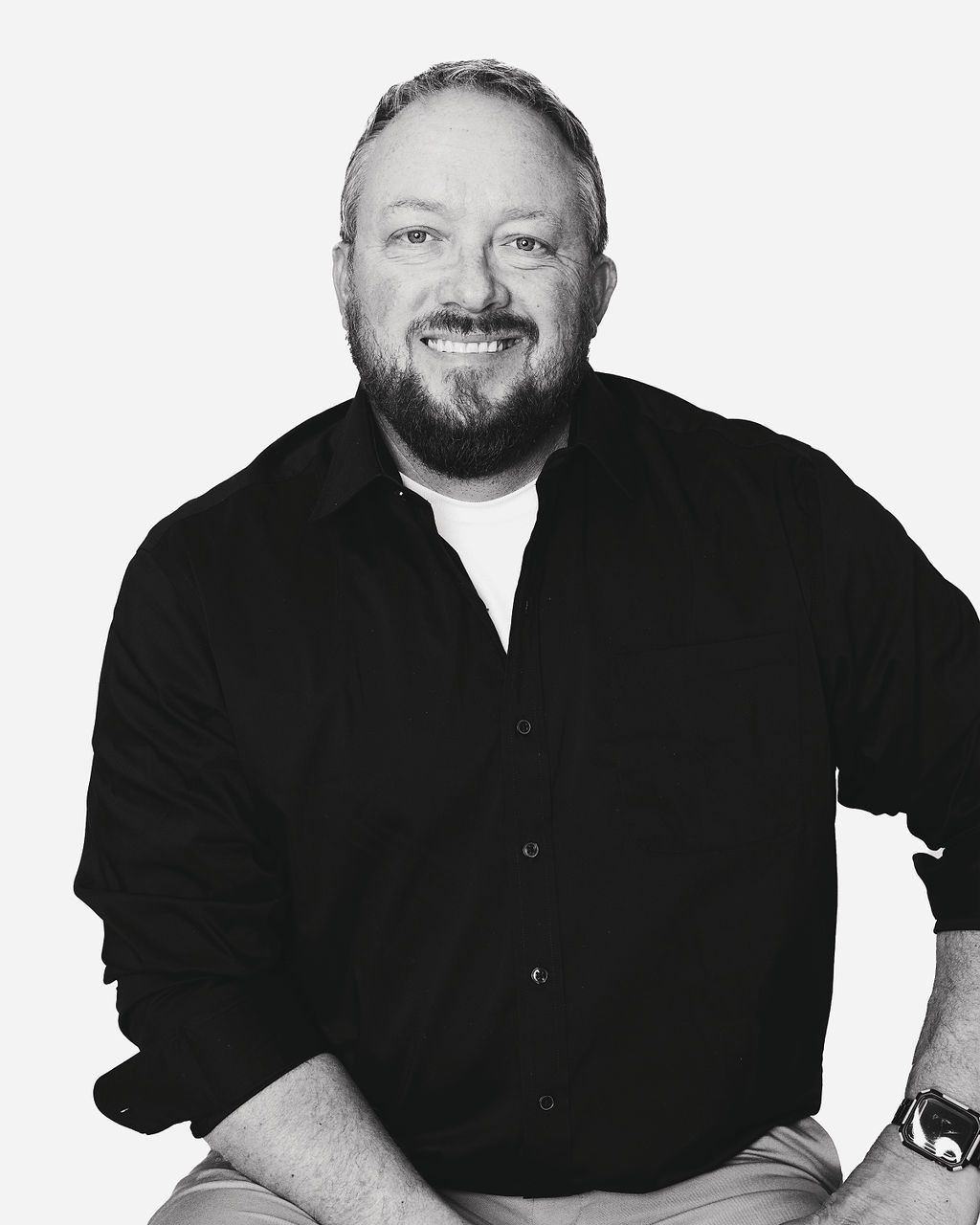 A man with a beard is wearing a black shirt and a watch