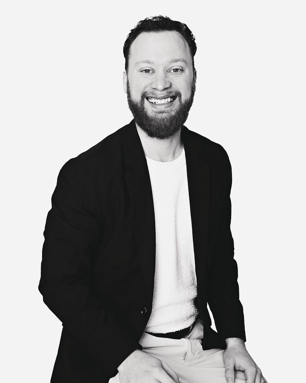 A man with a beard is smiling in a black and white photo.