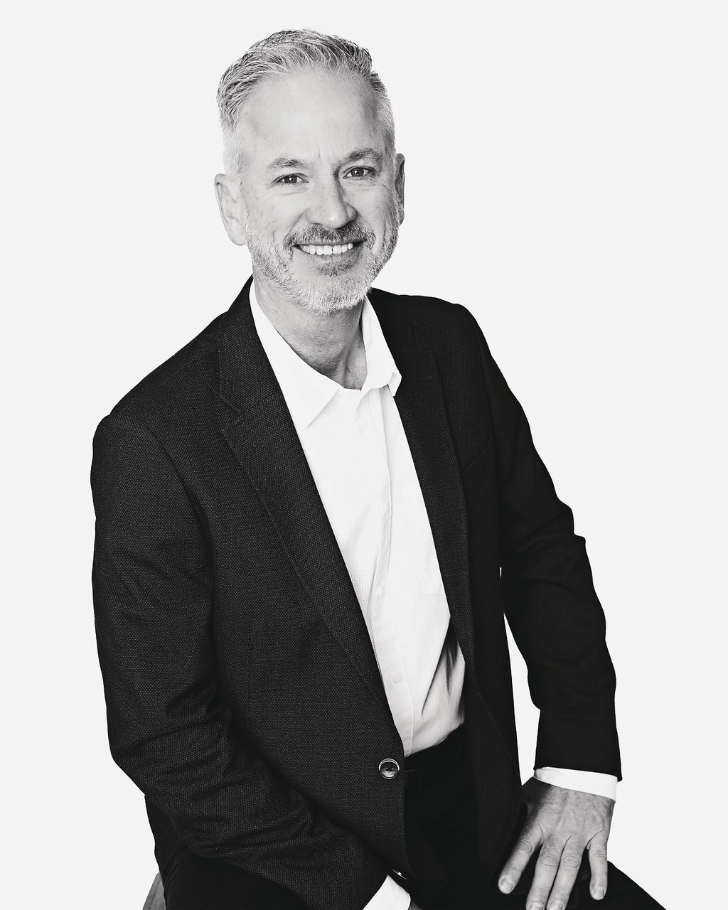 A man in a suit is sitting on a stool in a black and white photo.