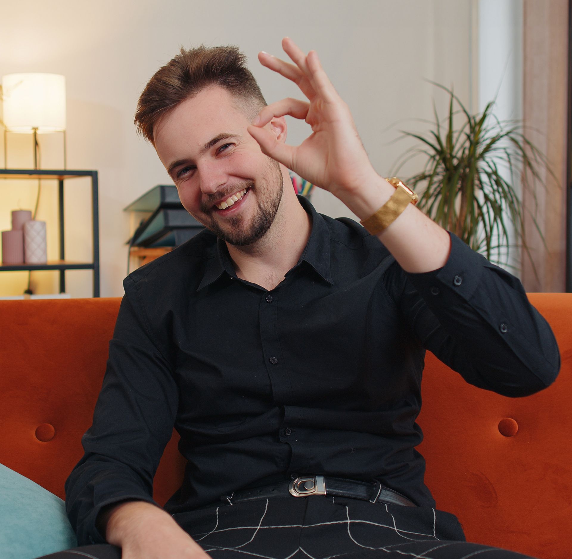 Man in black shirt on orange couch, giving 