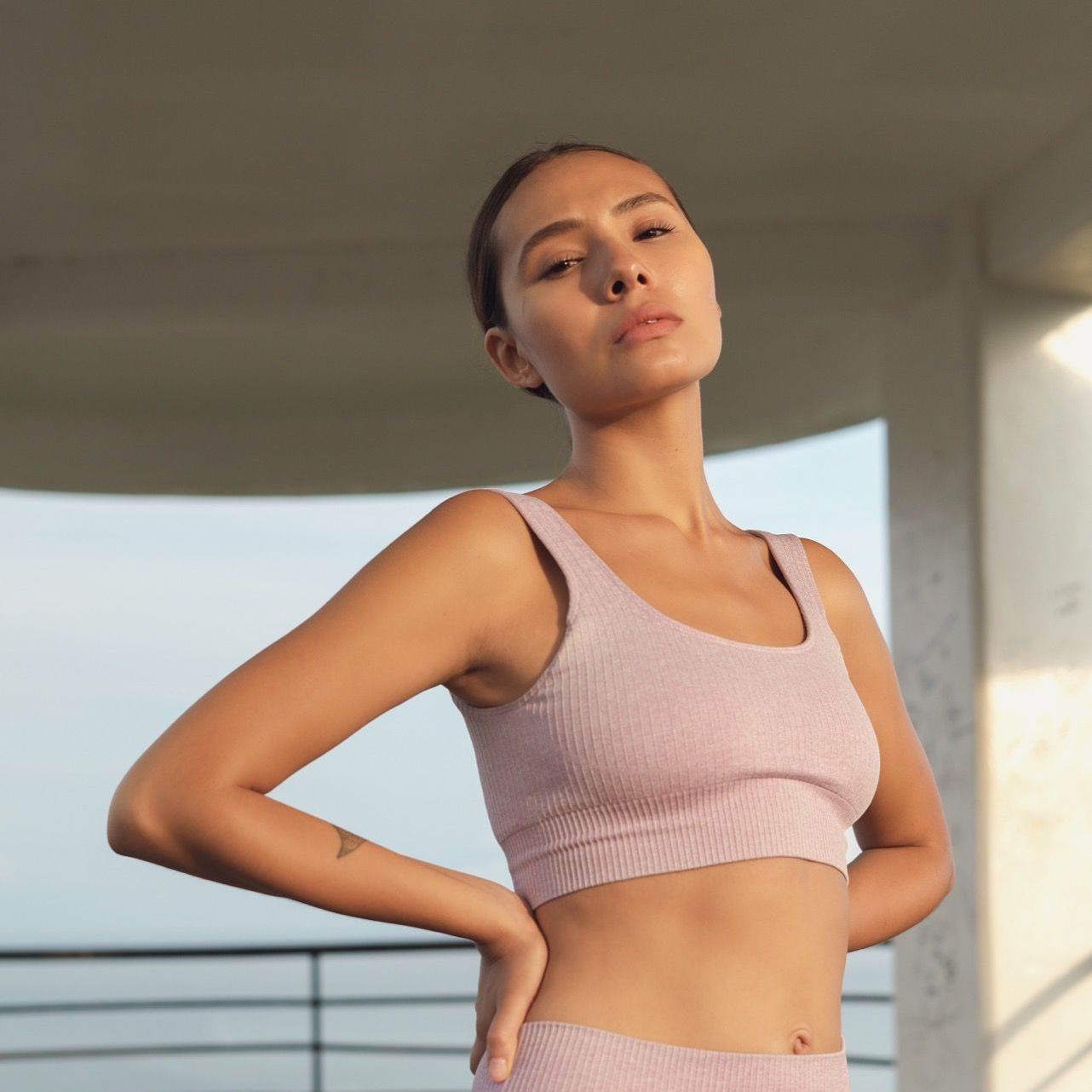 Woman in pink athletic top, hands on hips, under a white overhang.