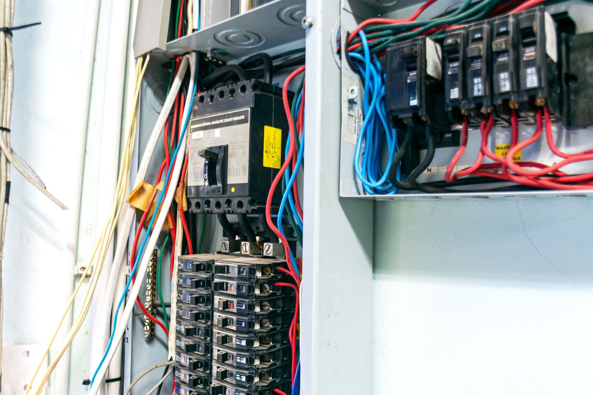 Electrical breaker panel with tangled red, blue, and white wires inside an open cabinet