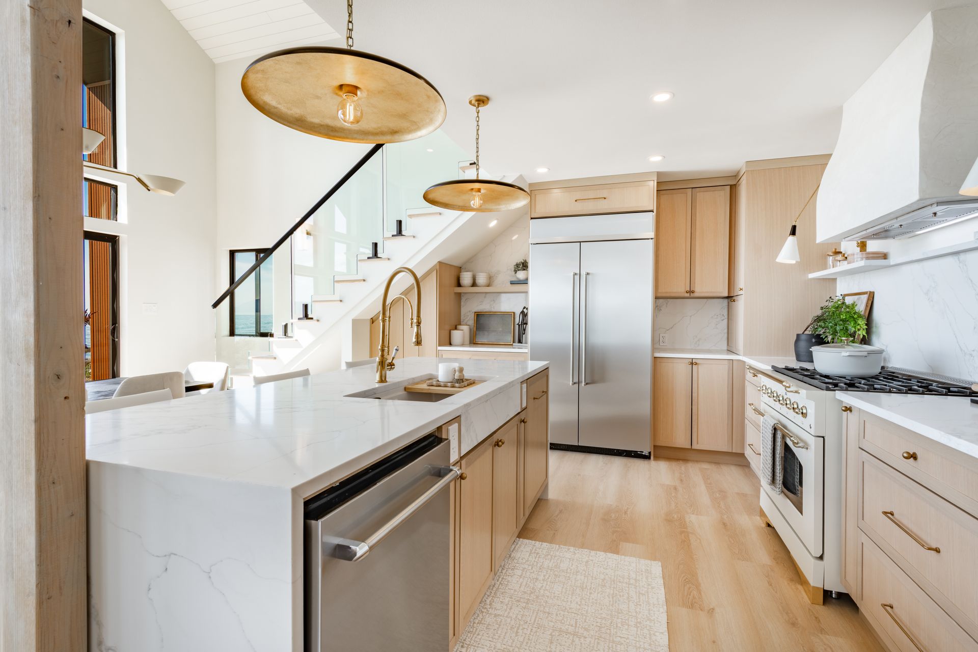 Bright modern kitchen with island, stainless steel appliances, and staircase in the background