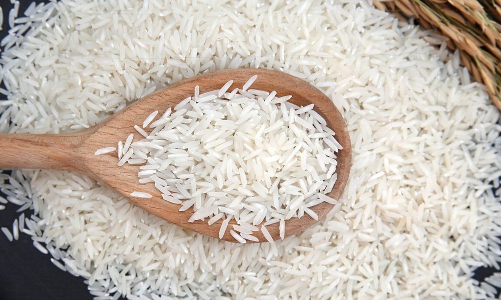 A wooden spoon filled with white rice is sitting on top of a pile of rice.
