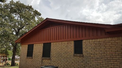 A brick house with a red roof and a tree in the background.