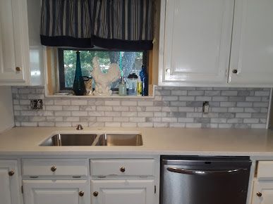 A kitchen with white cabinets , a sink , a dishwasher , and a window.