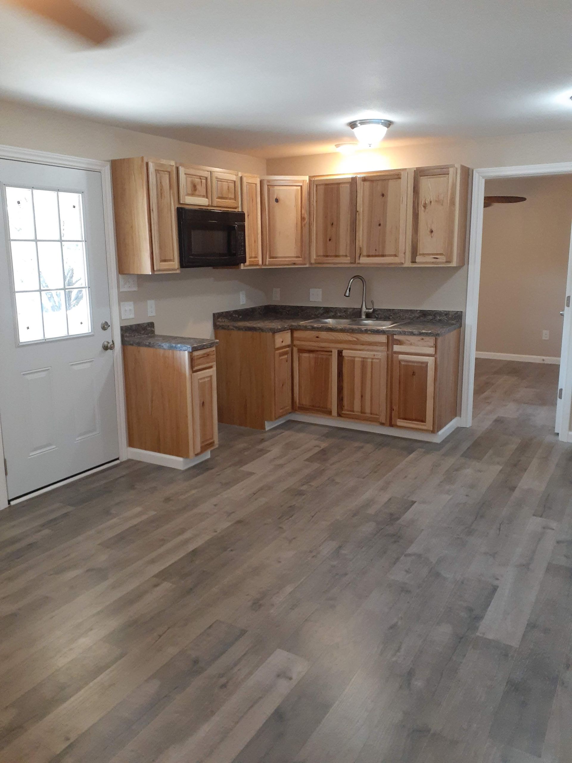 A kitchen with wooden cabinets , a sink , a microwave and a ceiling fan.