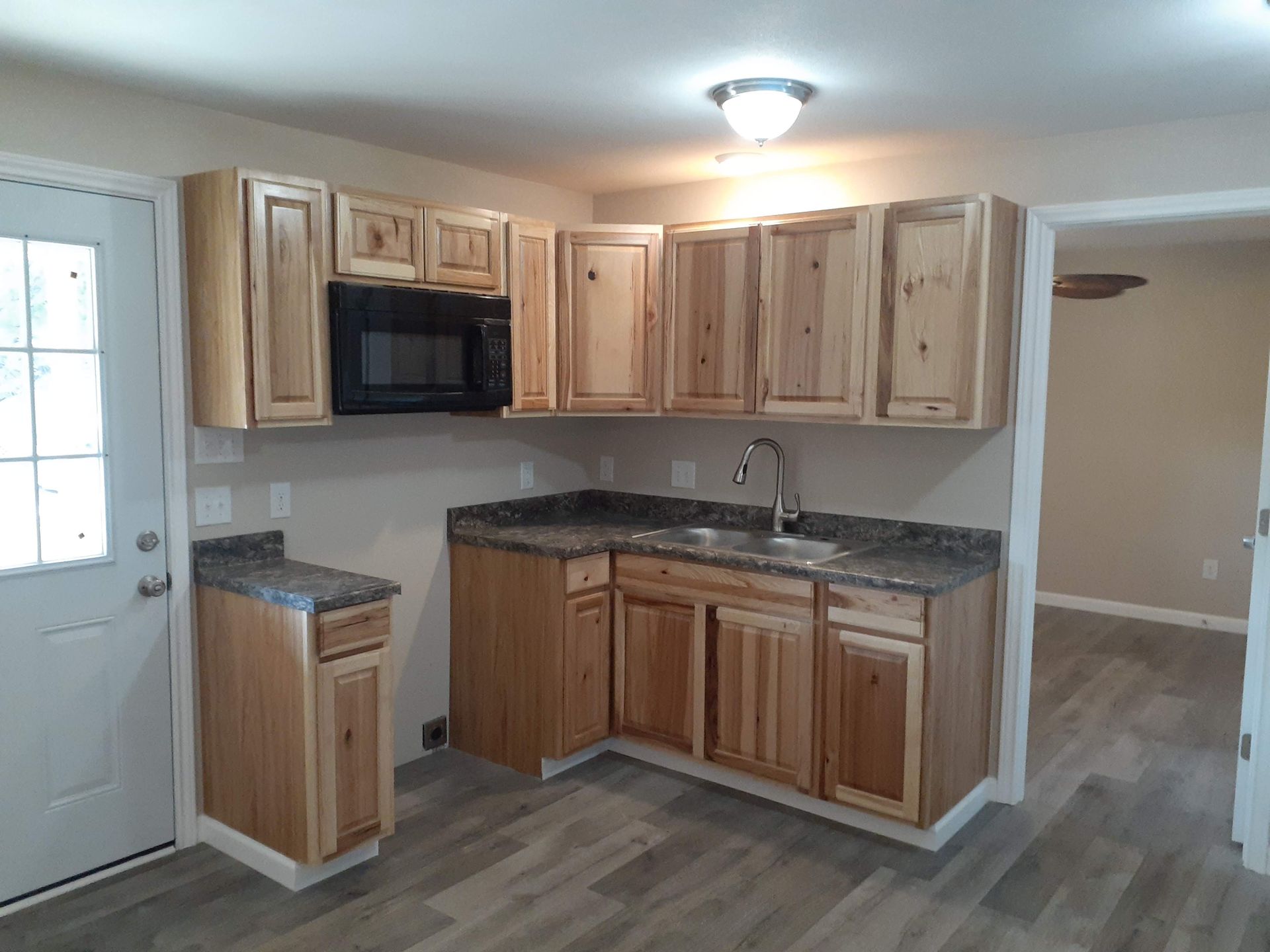 A kitchen with wooden cabinets , granite counter tops , a sink , and a microwave.