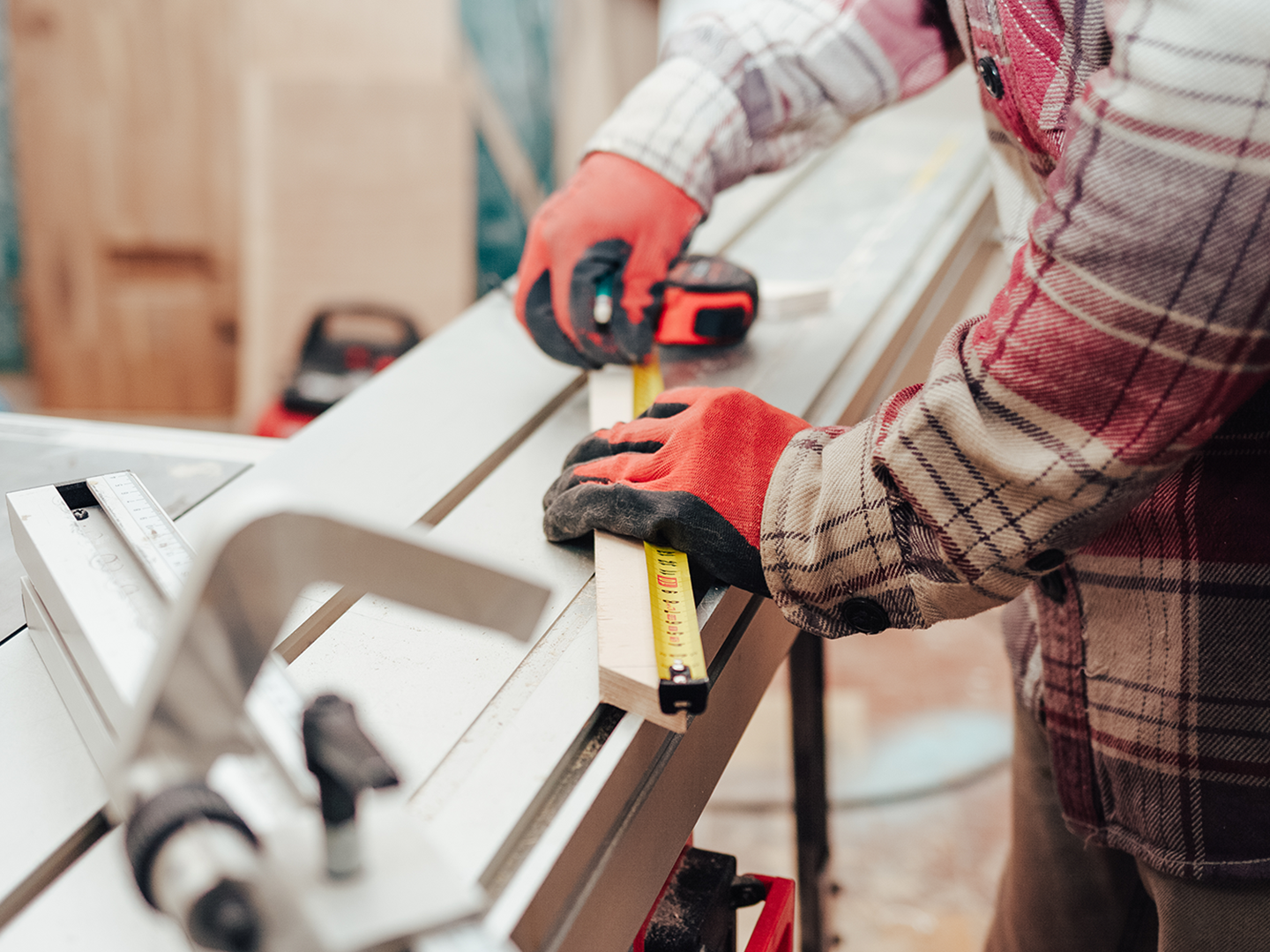 A man is measuring a piece of wood with a tape measure.