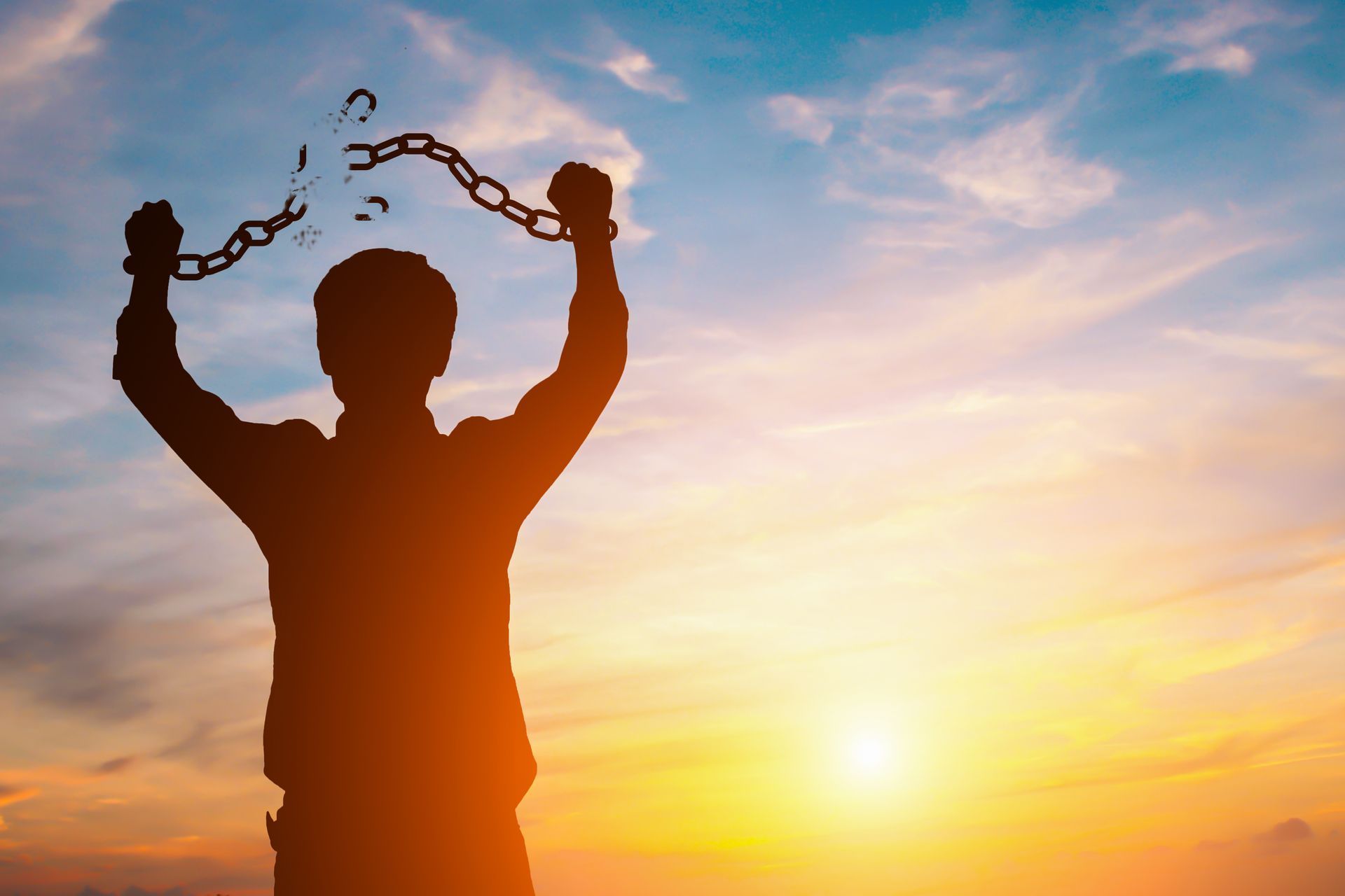 Businessman with broken chains in sunset.