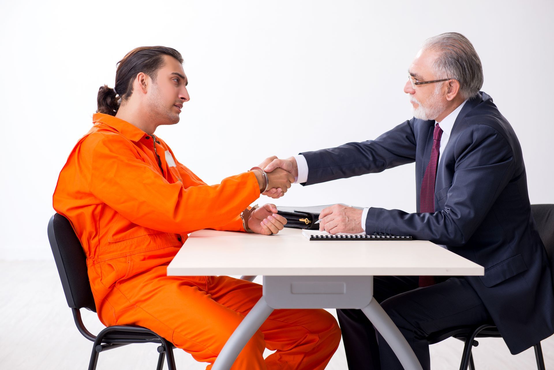 A person in an orange jumpsuit shaking hands with a person in a suit, at a table.