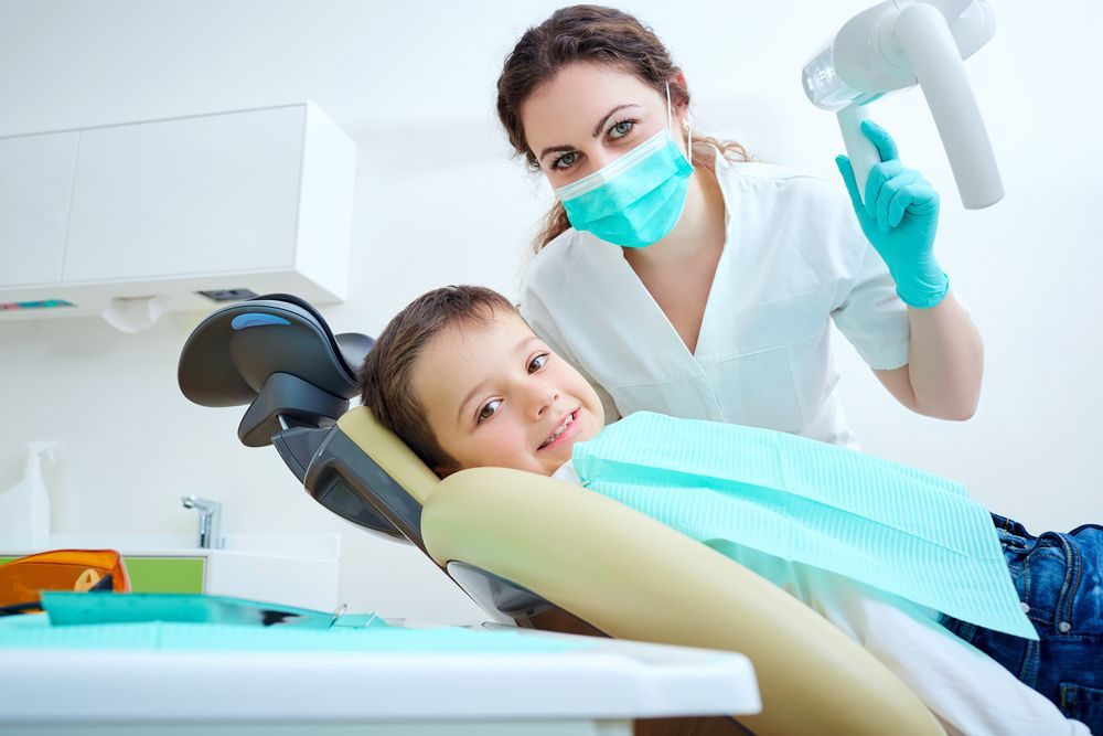 A Child in a Dentist Chair Smiles at the Camera as a Dentist Holds an X-ray Device — Tamworth Orthocare In Tamworth, NSW
