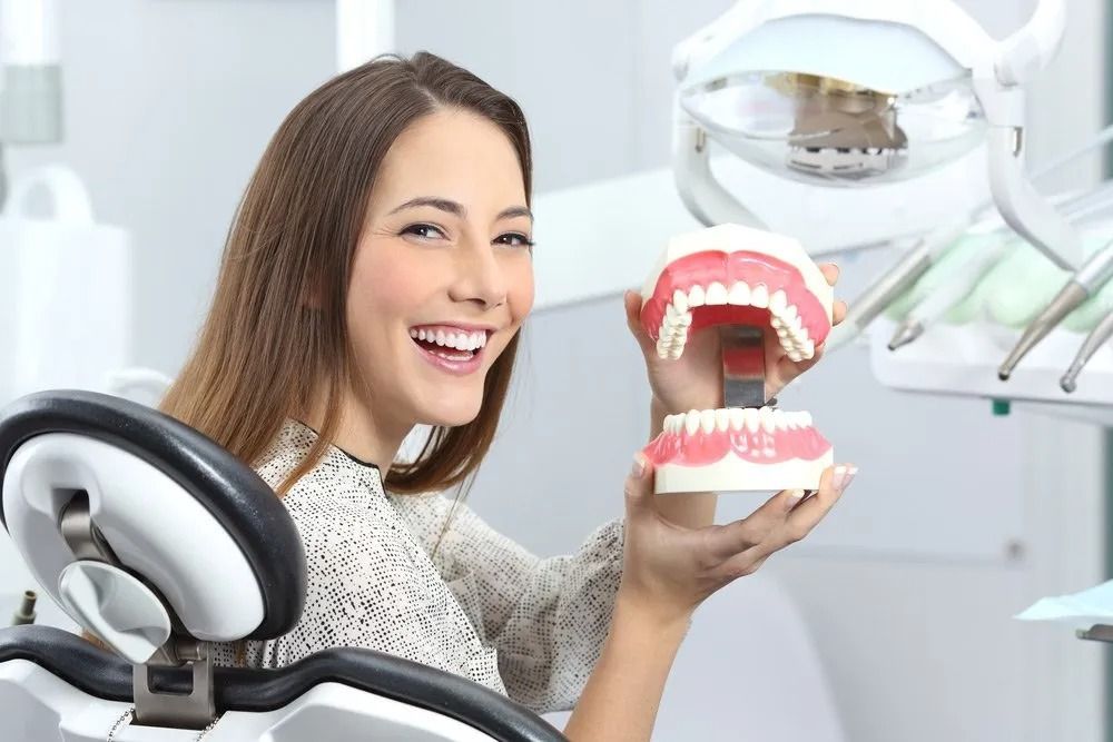 Woman in a Dental Chair Smiles, Holding a Model of Teeth — Tamworth Orthocare In Tamworth, NSW