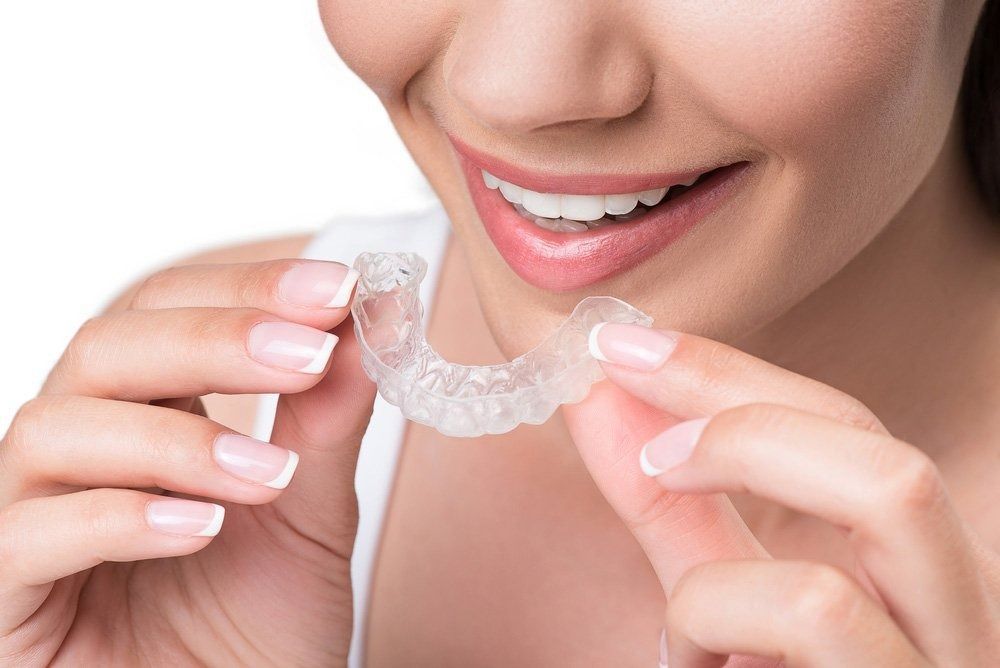 Woman Smiling, Holding a Clear Dental Aligner — Tamworth Orthocare In Tamworth, NSW